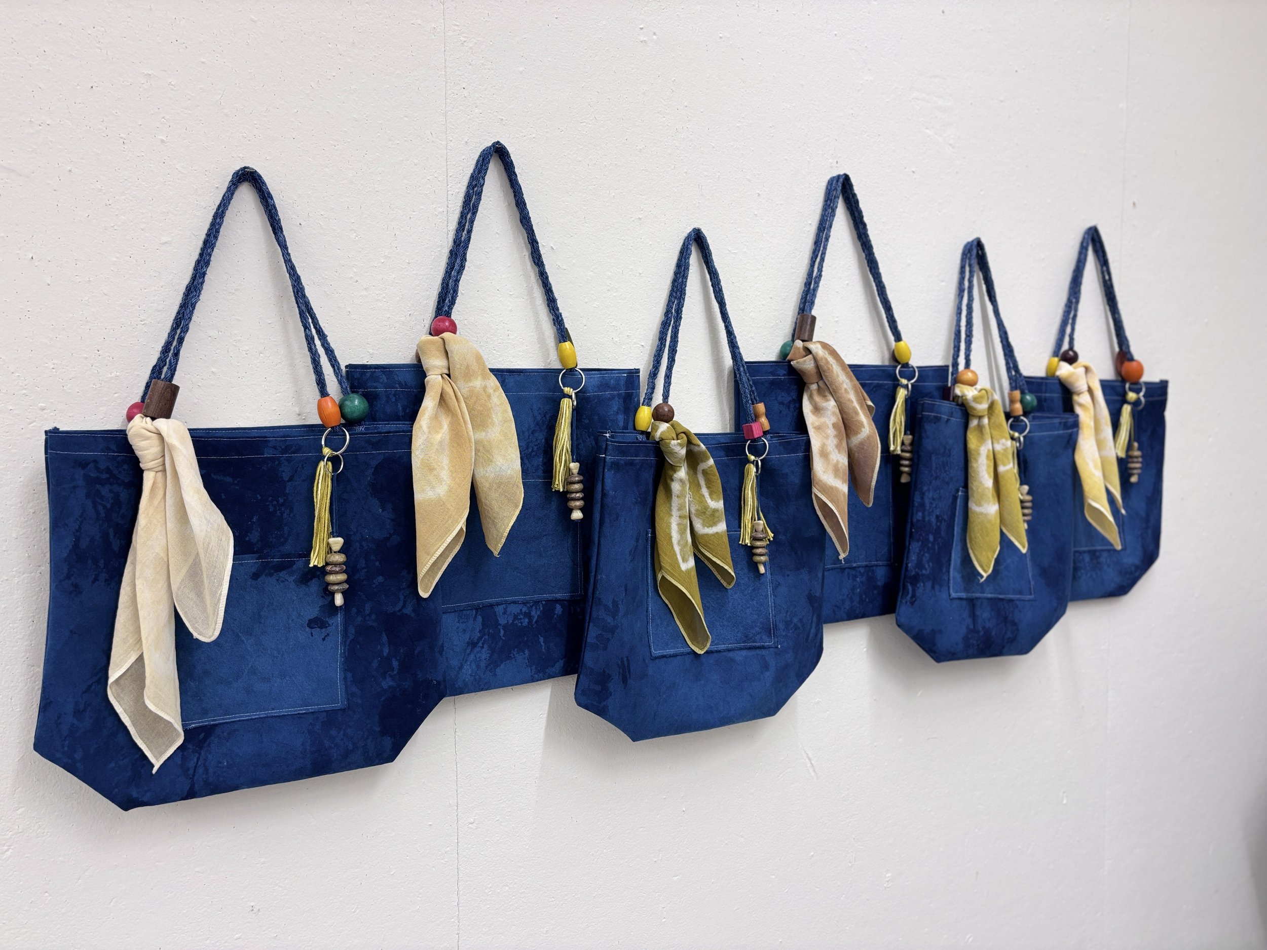 Alexis Fredericks, WORKING CLOTH., six handcrafted textile bags displayed as an installation, exploring the relationship between institutional affiliation, artistic labor, and professional recognition.