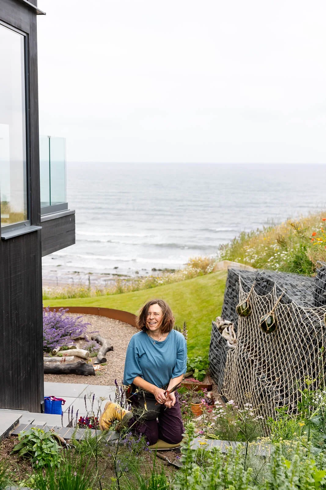 clare kneeling in plant bed working on plants with the north sea in the background