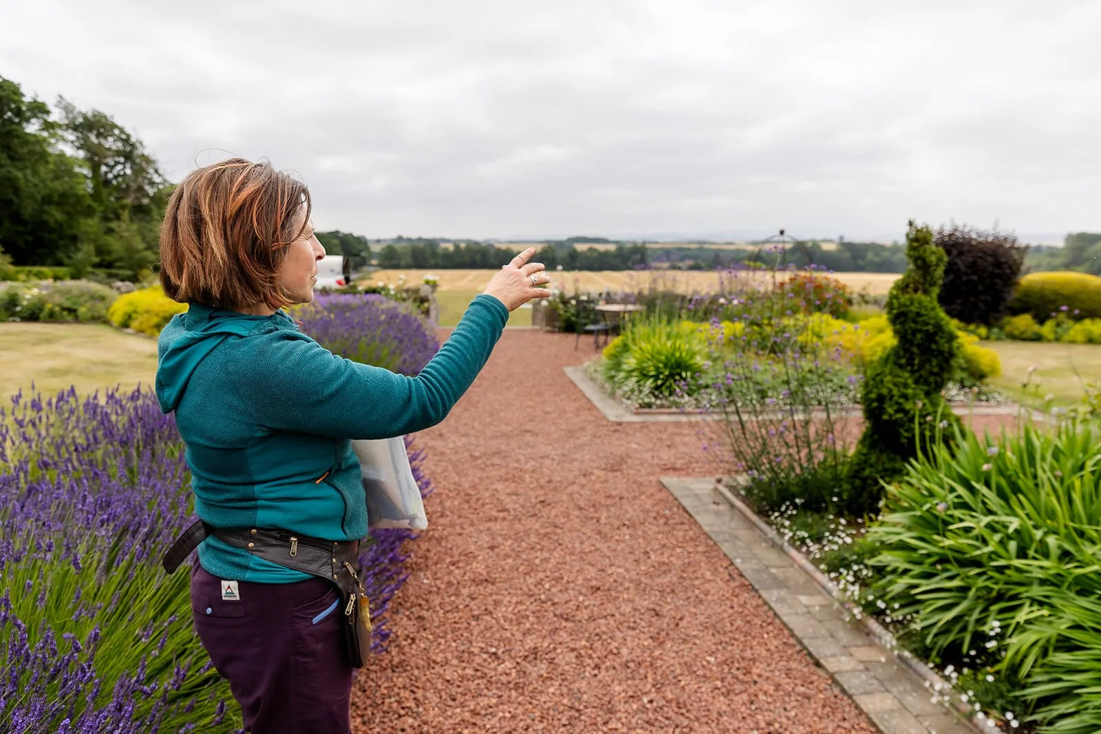 clare pointing to a spot in the garden she is standing on gravel pathway to view in background