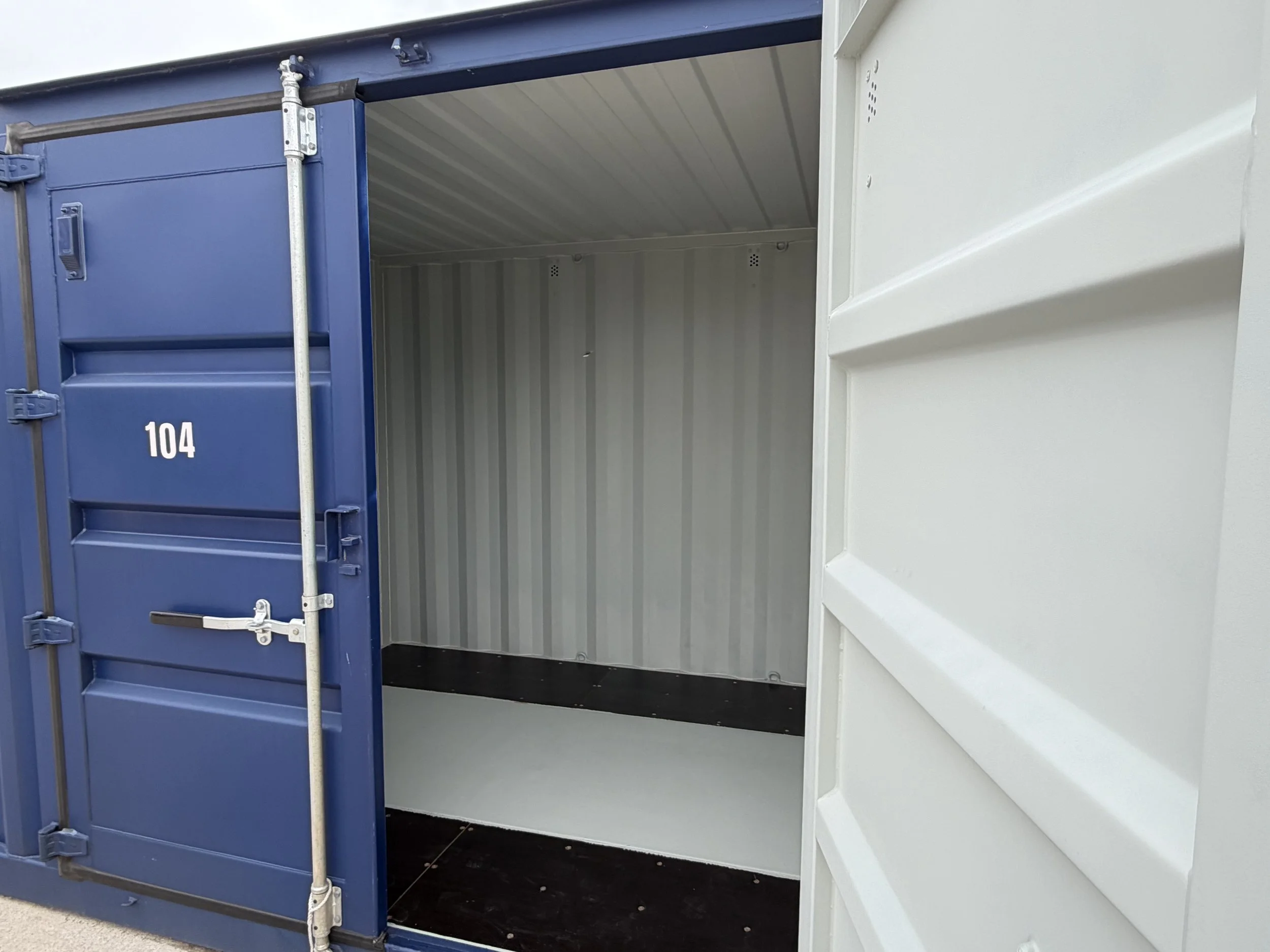 Empty shipping container with blue door open, white interior, and black floor.