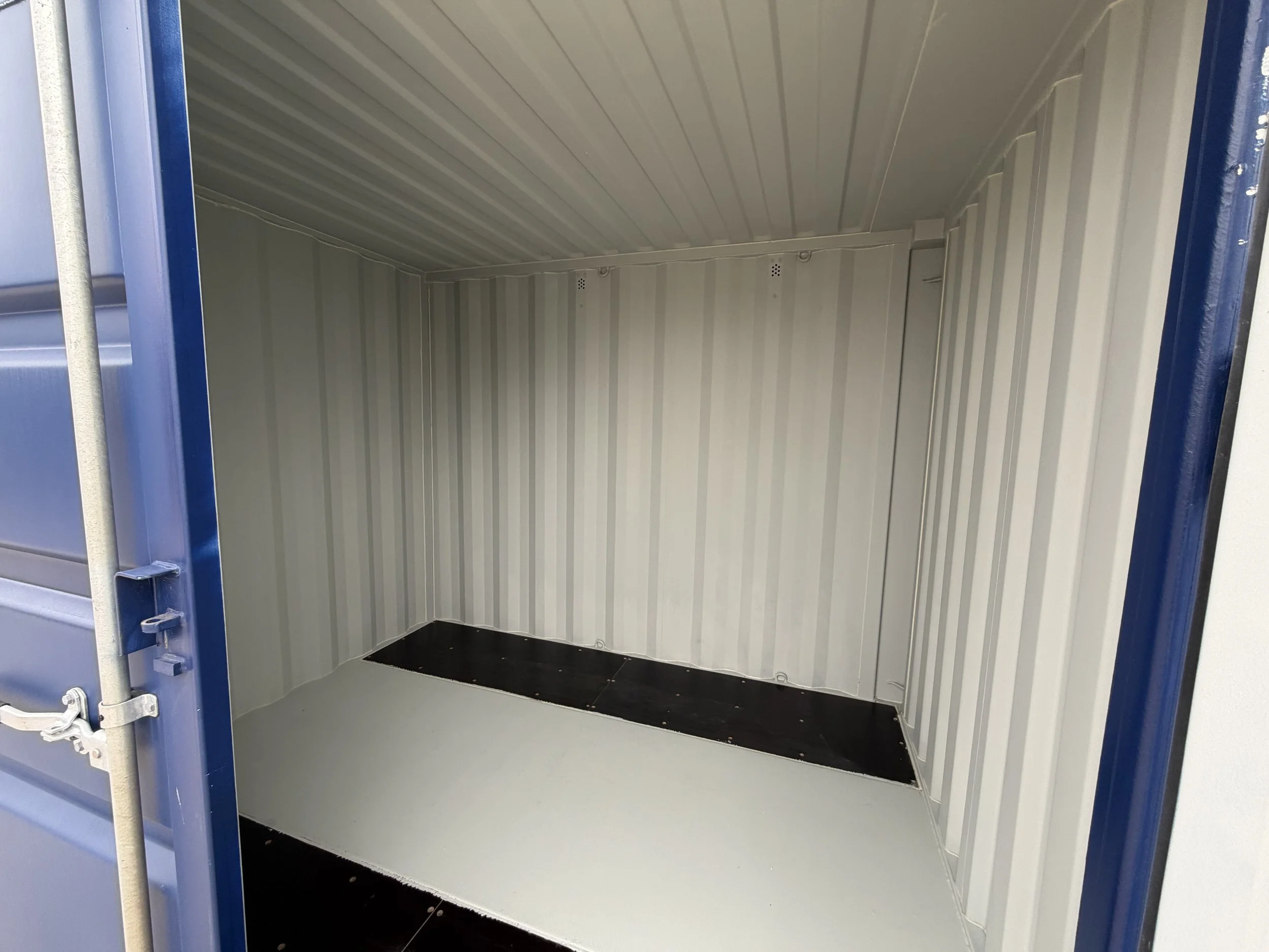 Empty blue shipping container with white interior walls and black flooring.