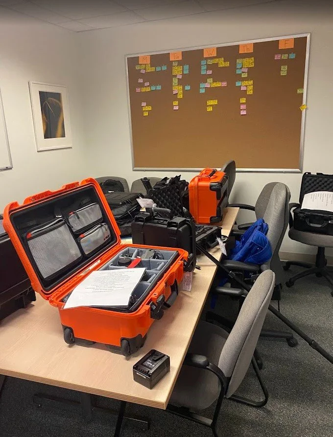 Conference room with equipment cases on the table and a large bulletin board with colored notes in the background.