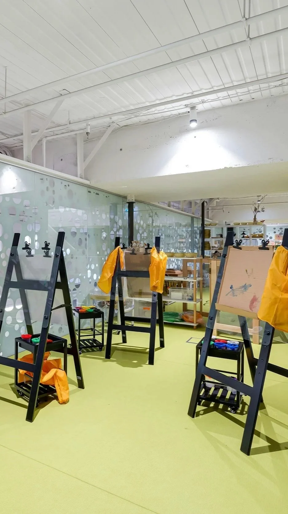 Art classroom with paint easels, supplies, and a bright yellow floor.