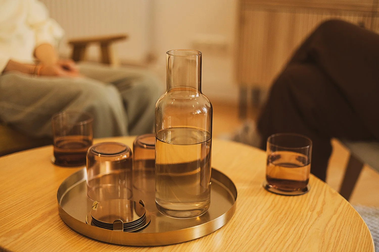 Ein runder Holztisch mit einer silbernen Kanne und vier gefärbten Gläsern, die mit Wasser gefüllt sind.