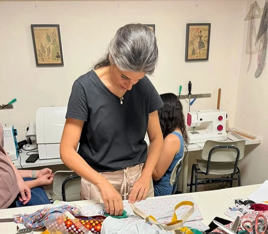 Gili Azran working on a sewing pattern with fabric and measuring tools at Gili Studio in Jerusalem.