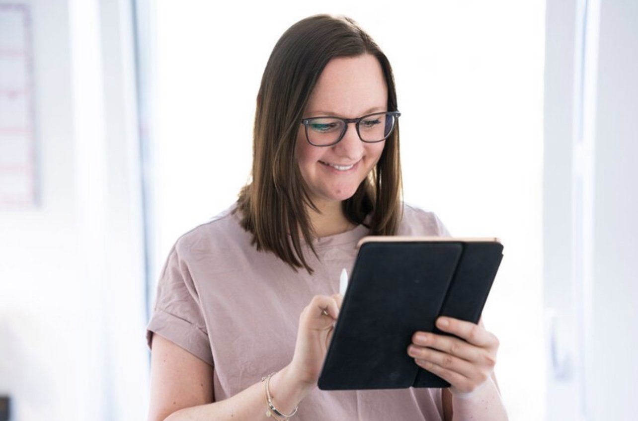 Frau mit Brille nutzt ein Tablet in einem hellen Raum.