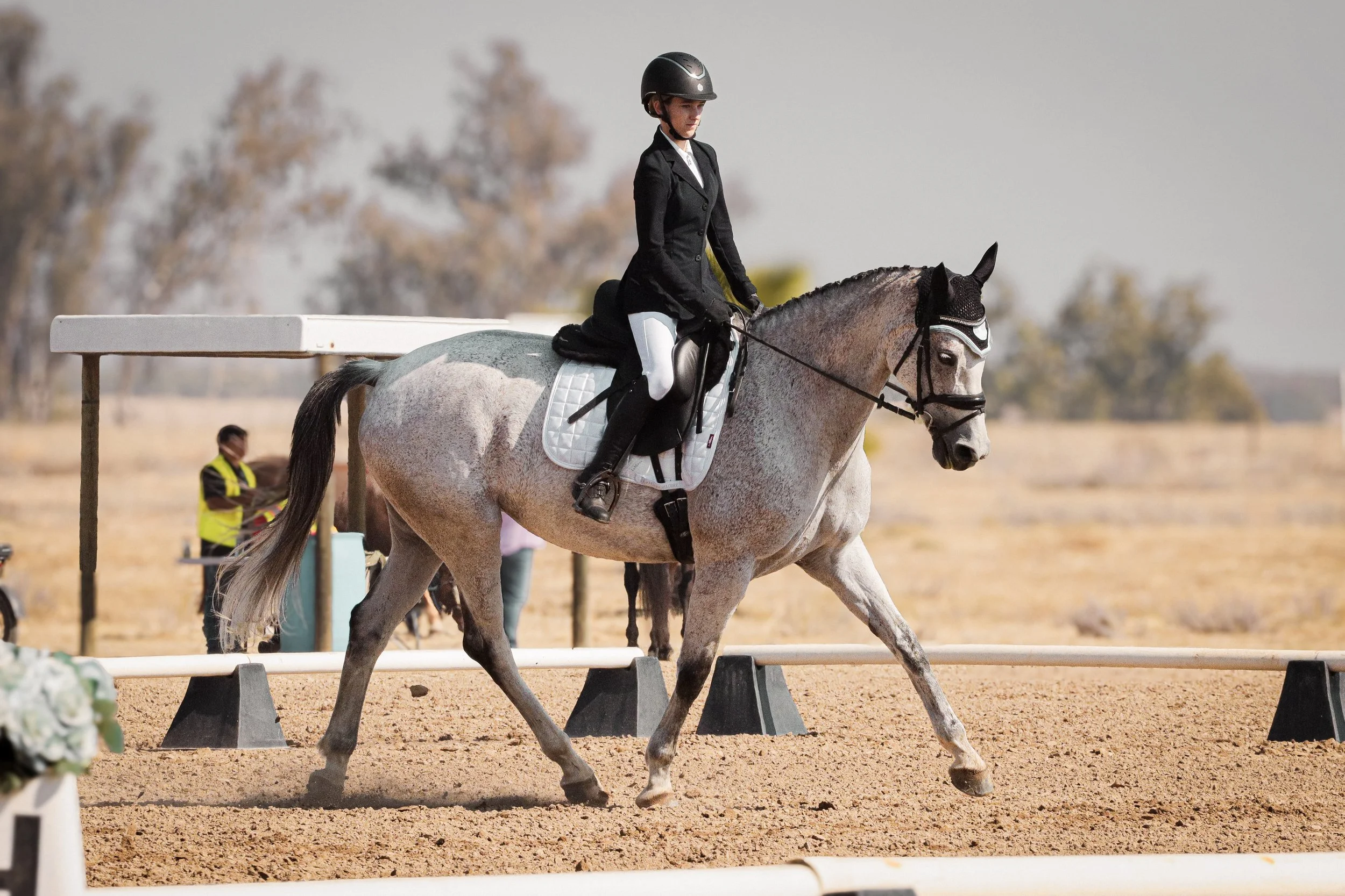 A person riding a gray horse wearing a black helmet and black riding jacket during an equestrian event.