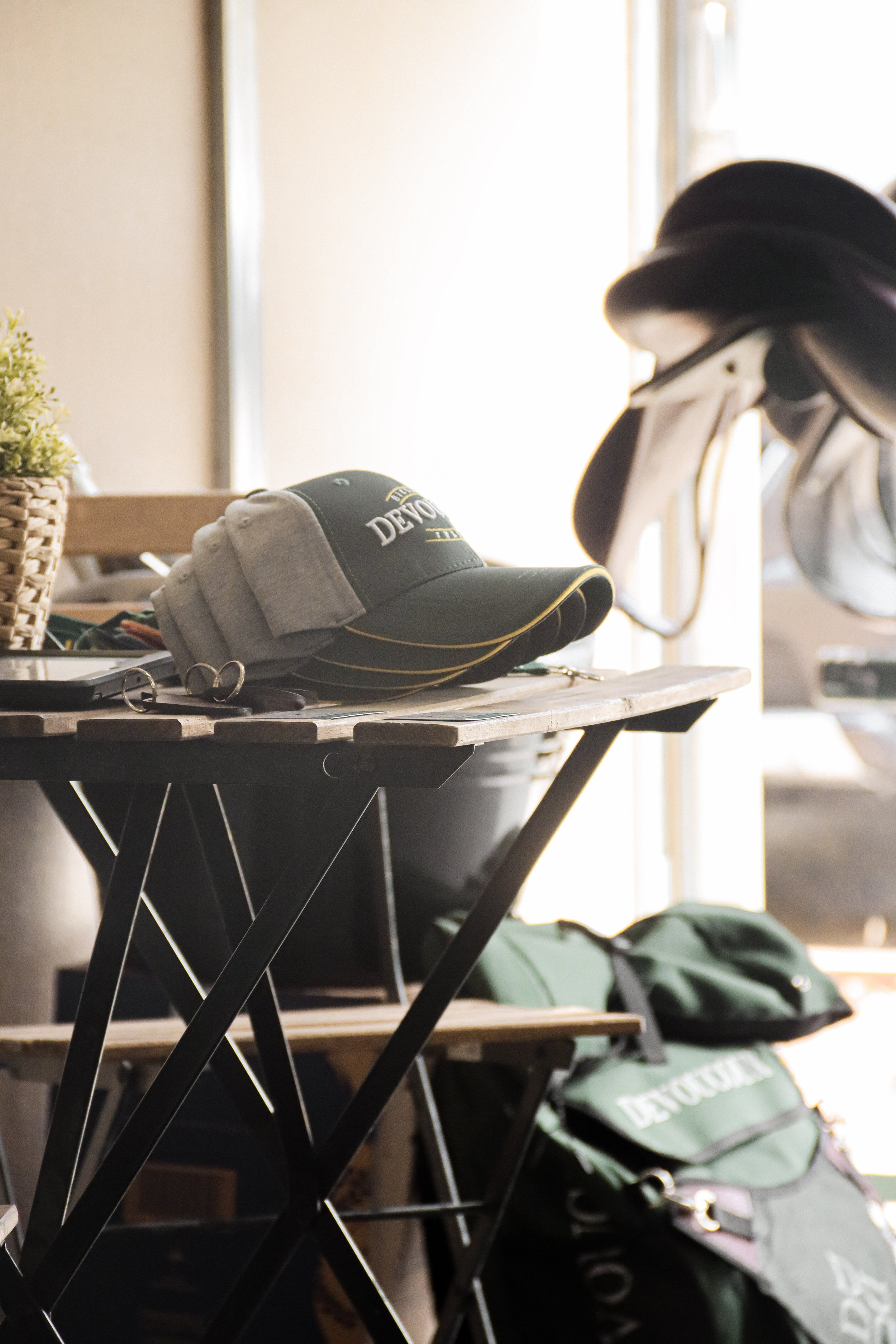 A wooden table with various golf accessories, including a baseball cap, sunglasses, and golf clubs in a storage bag. Behind the table, there is a window with bright sunlight coming through.
