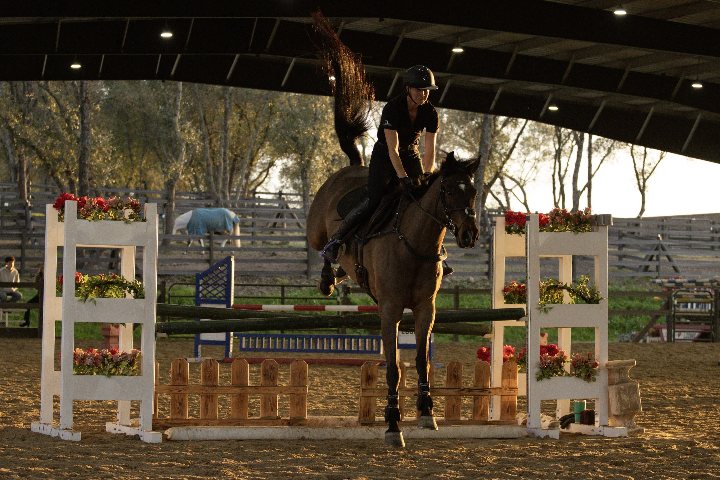 A person riding a horse over an obstacle during sunset at an equestrian competition.