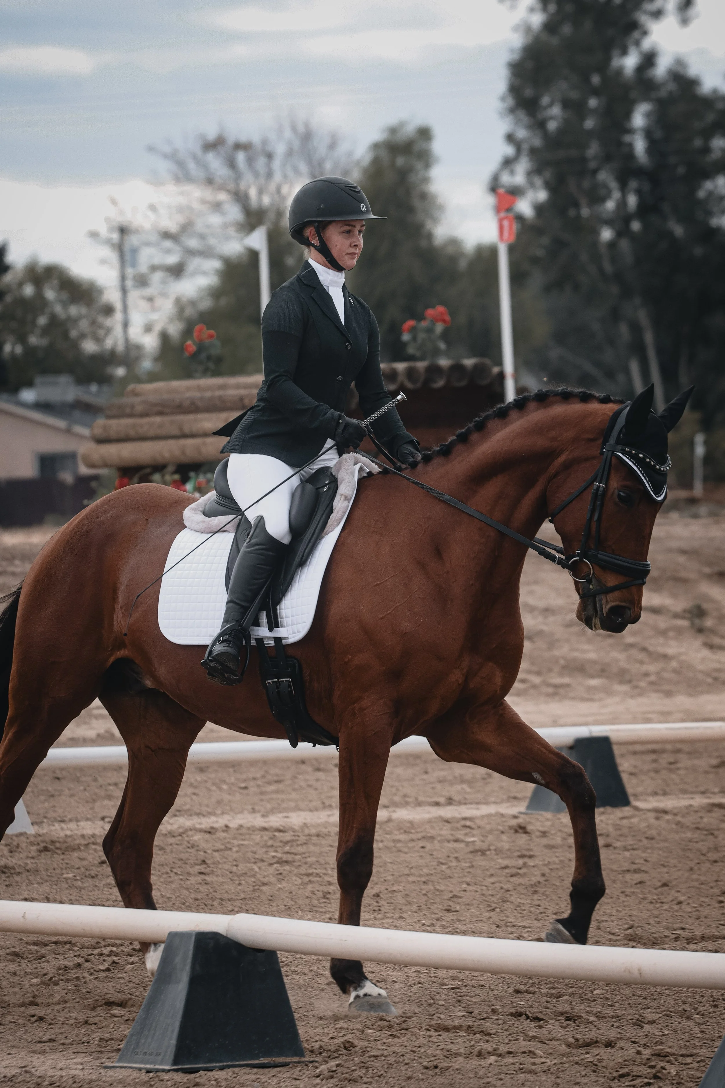 A woman riding a brown horse during an equestrian event, wearing a black helmet and riding attire. She is holding the reins and has a focused expression.