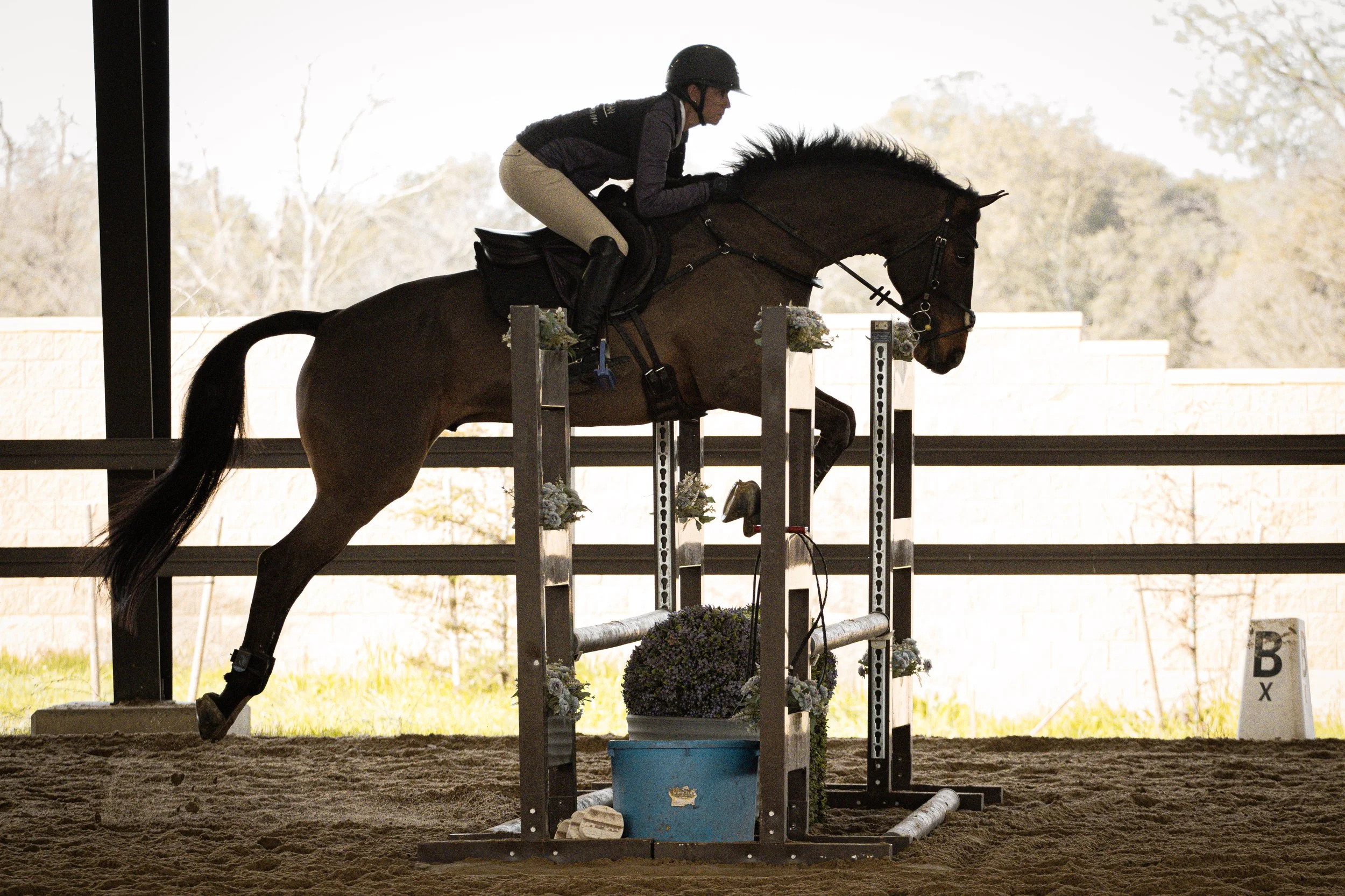 A person riding a horse jumping over an obstacle during an equestrian event inside an indoor arena.