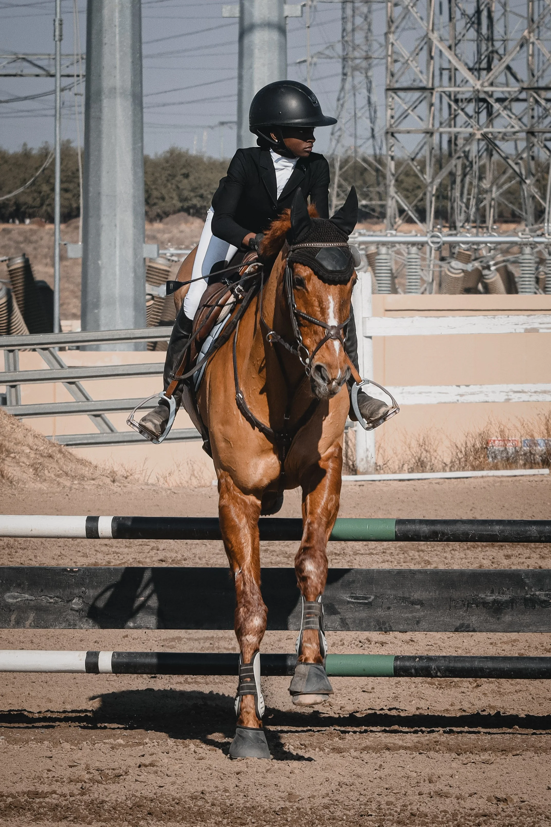 A rider wearing a black helmet and black jacket riding a brown horse over a jump on an equestrian course.