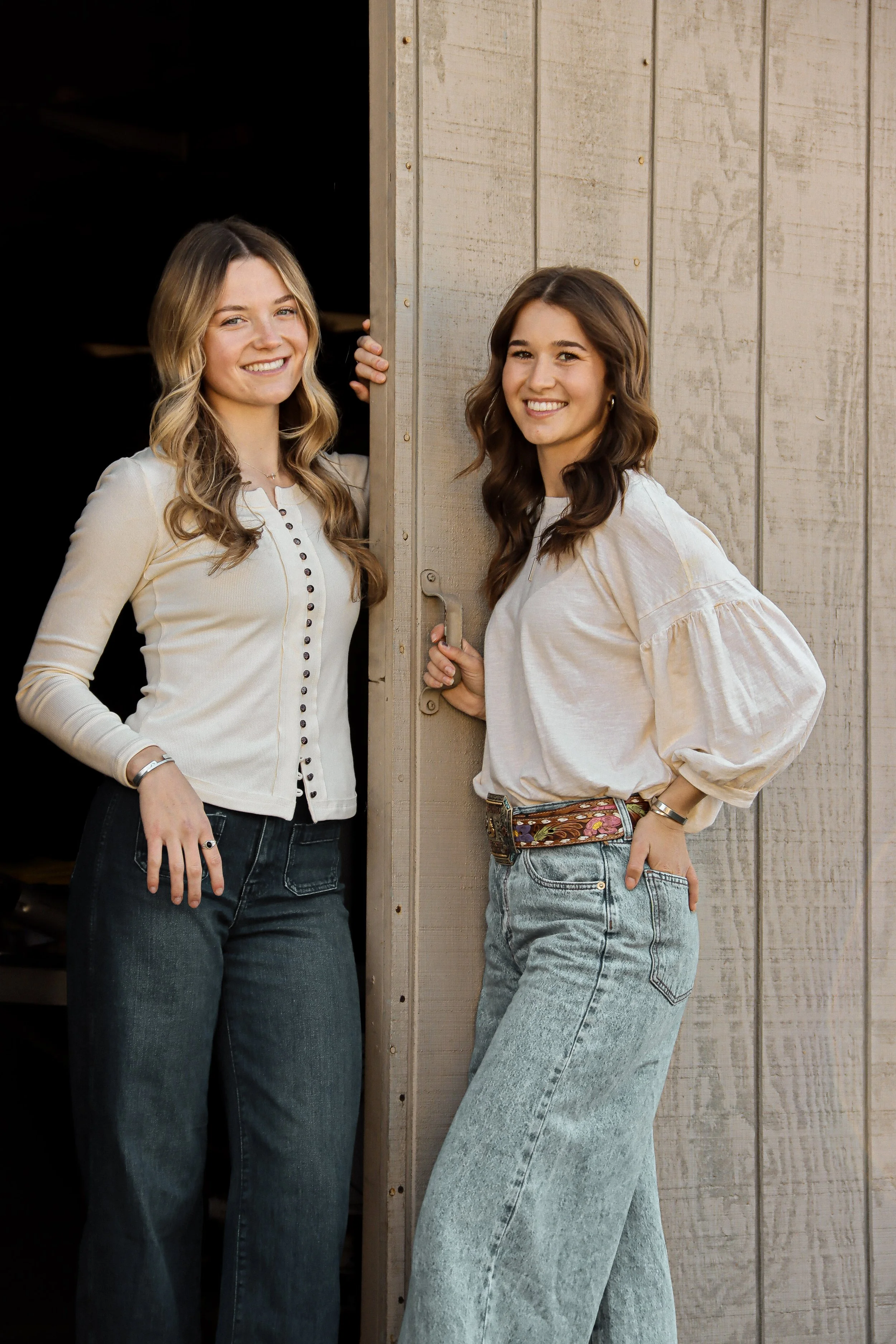 Two young women smiling and standing by a wooden door on a wooden wall, one on each side.