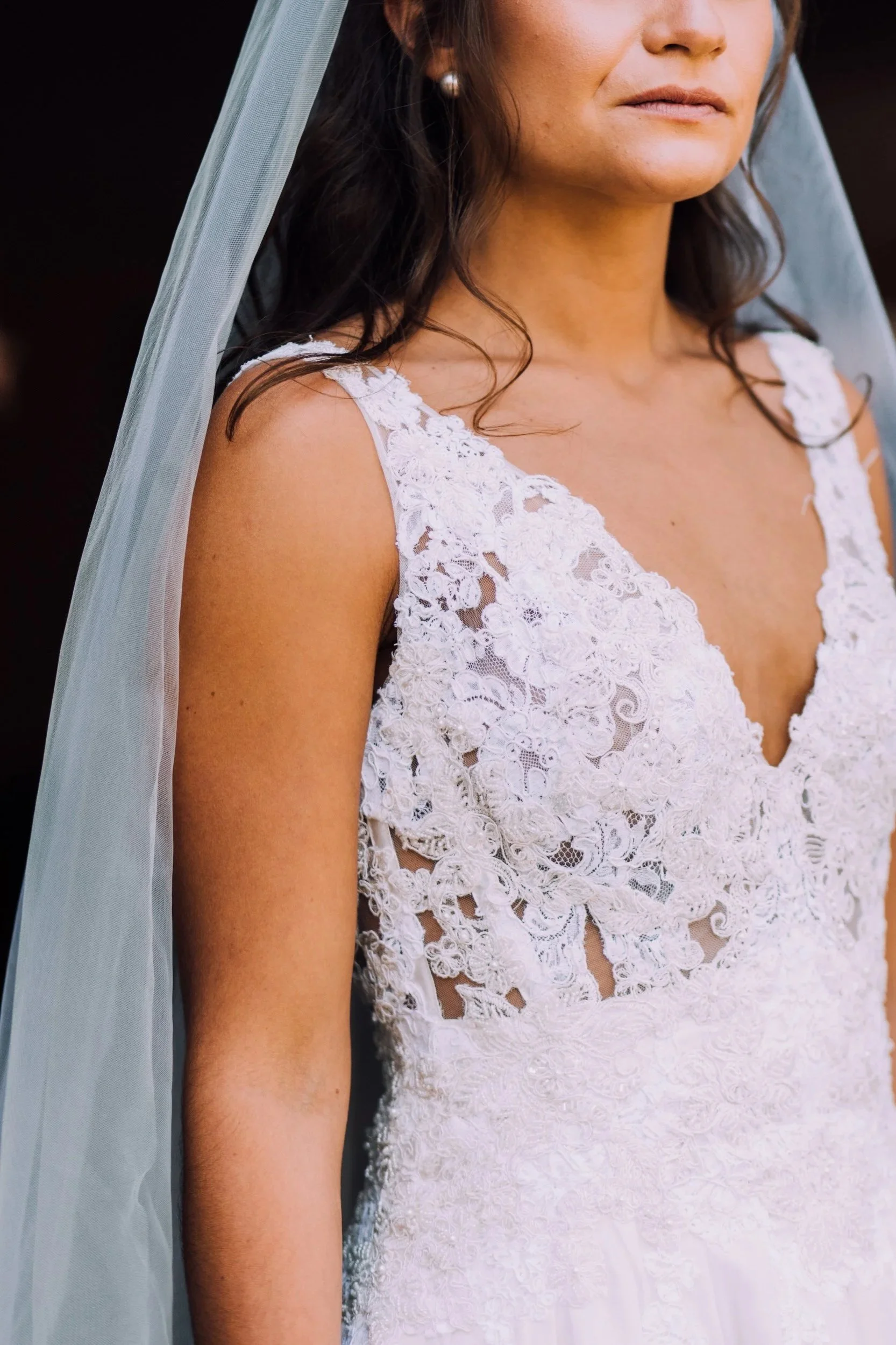 Close-up of a woman in a white lace wedding dress with a veil and pearl earrings.