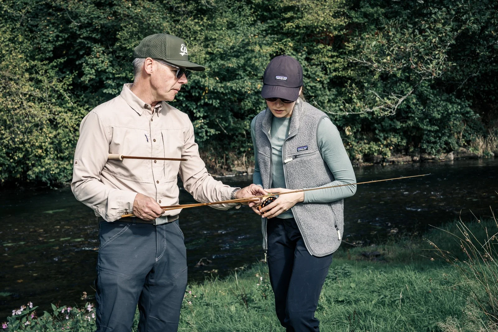 Two anglers learning to use a fly-fishing rod beside a wooded stream