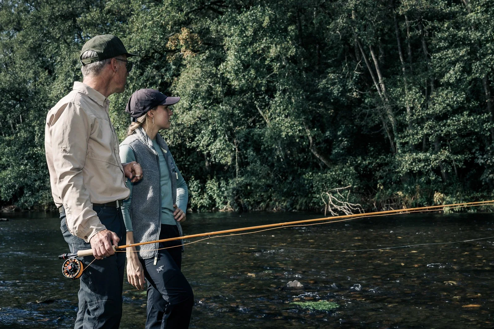 Two anglers holding fly-fishing rods while standing in a wooded stream