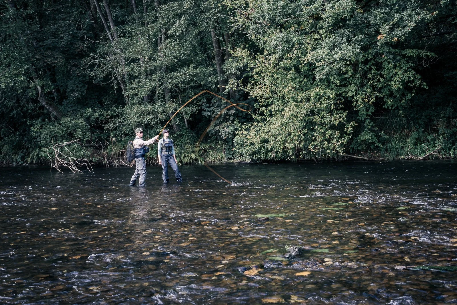 Two fly fishermen wading in a shallow forest stream