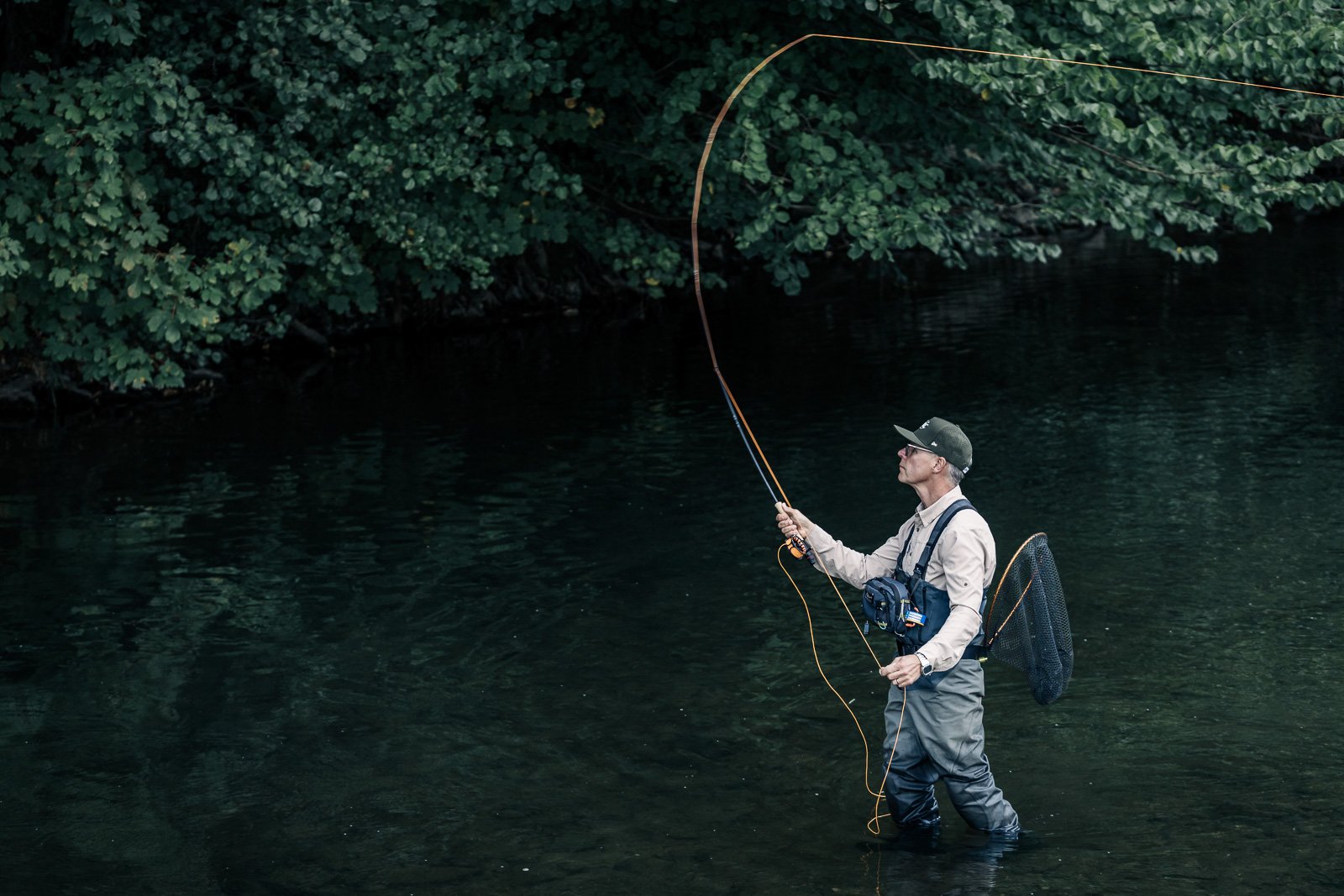 Fly fisherman wading in a forested river with a cast fishing line