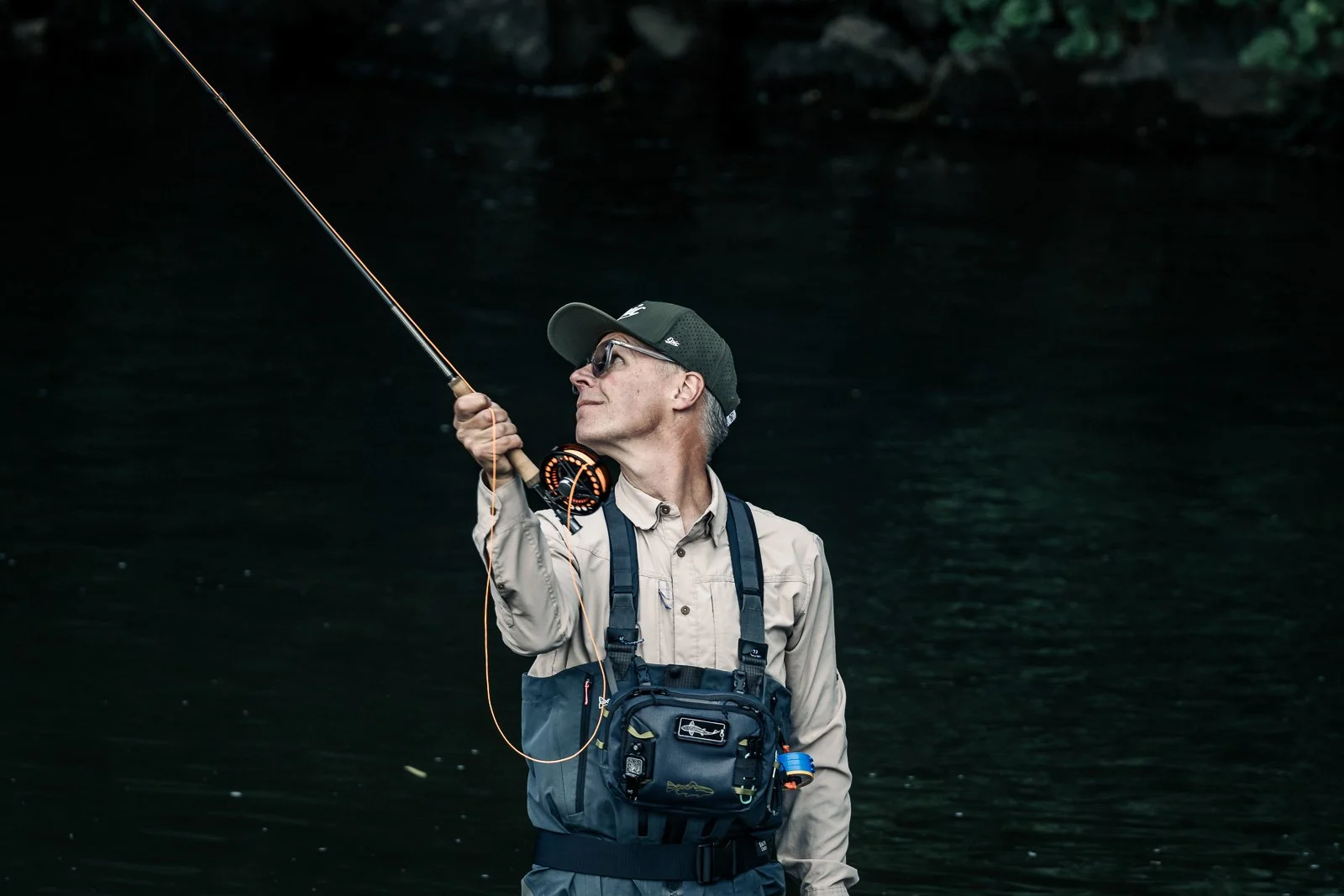 Fly fisherman in waders casting a fishing rod over a dark river
