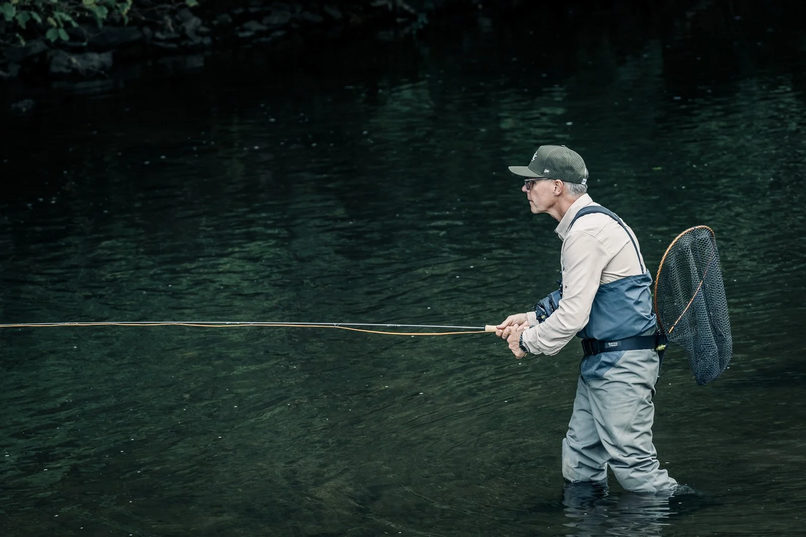 Fly fisherman wading in a river with a fishing rod and landing net