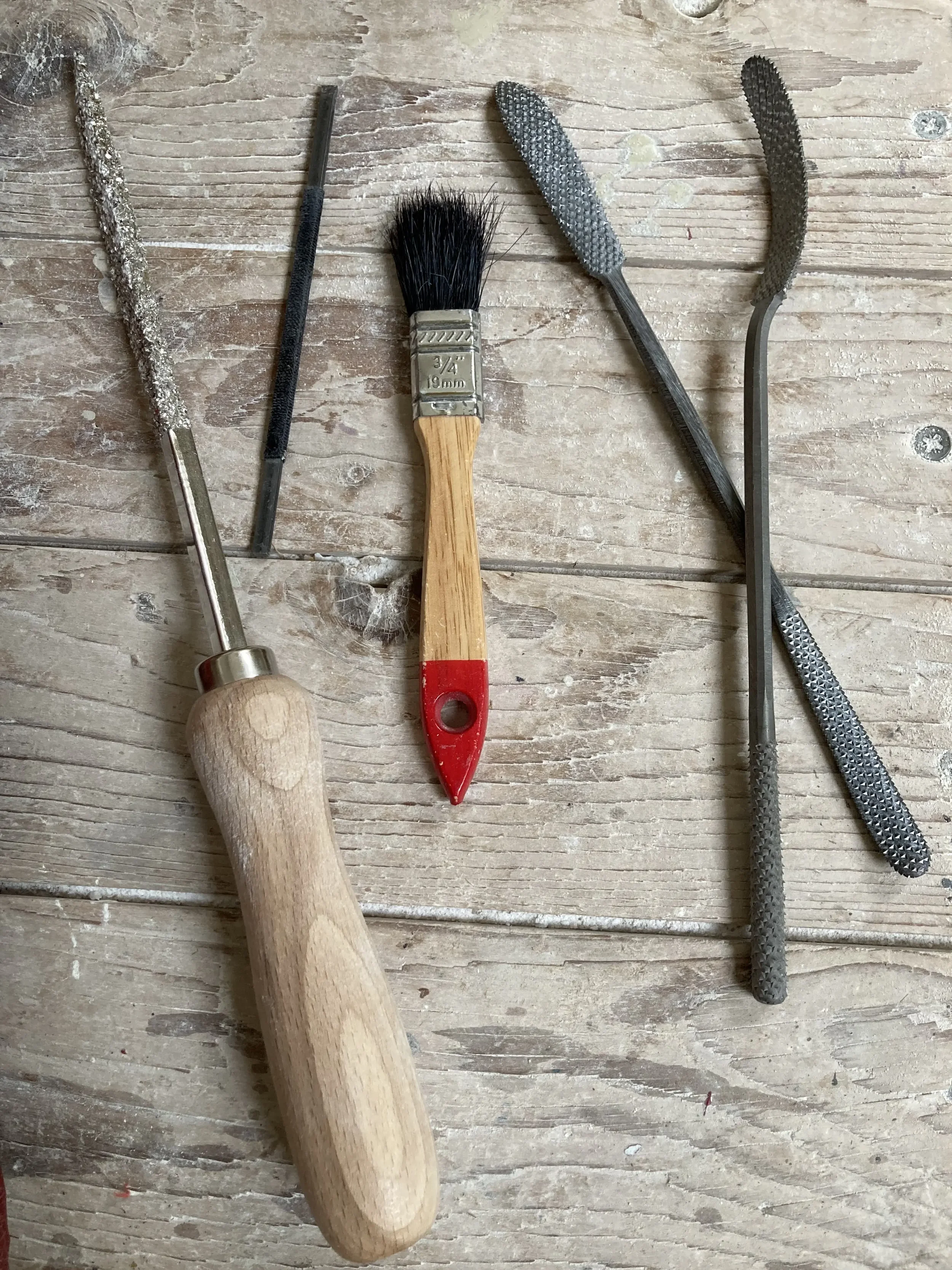 Beeldhouwgereedschap, raspen, een beiteltje en een zachte kwast gelegen op een houten tafel.