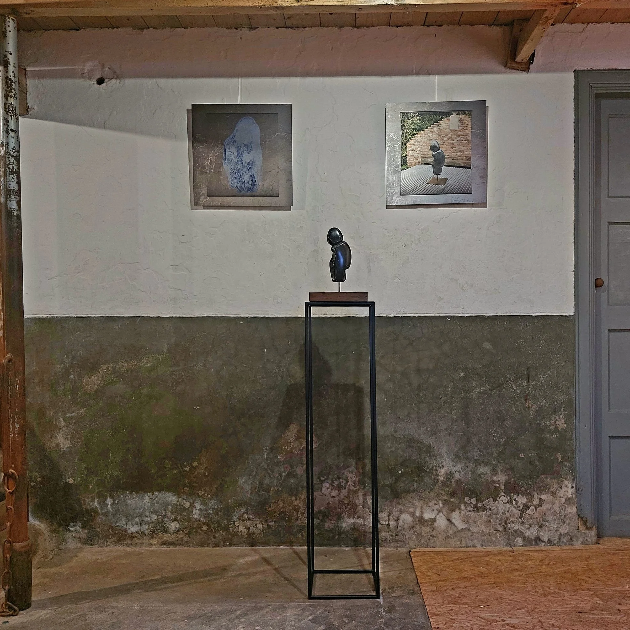 Beeld Denken op een zwarte metalen sokkel tegen een witte grijze achtergrond met twee foto's op aluminium van de ruwe steen en het beeld zelf