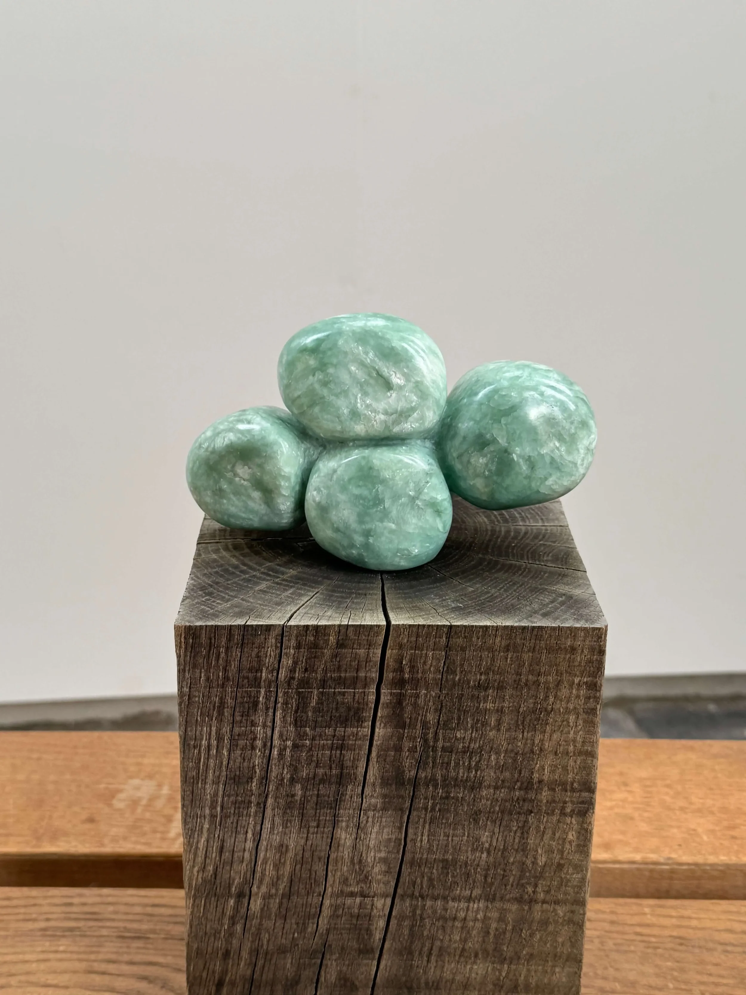 Beeld van groene speksteen met vier bolletjes dicht tegenelkaar aan, op een houten sokkel..
