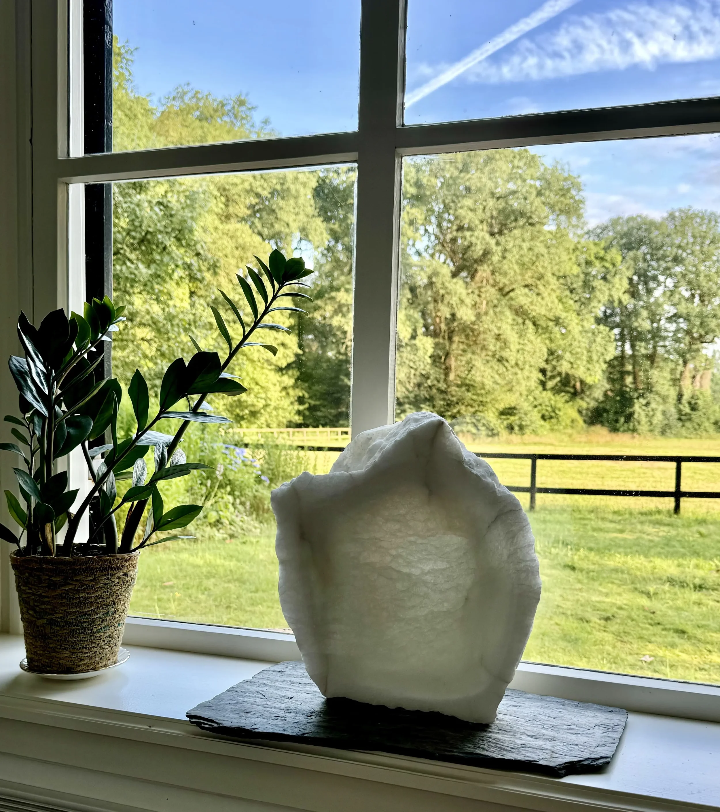 Wit albasten staand beeld in een vensterbank, het licht maakt het albast bijna transparant.