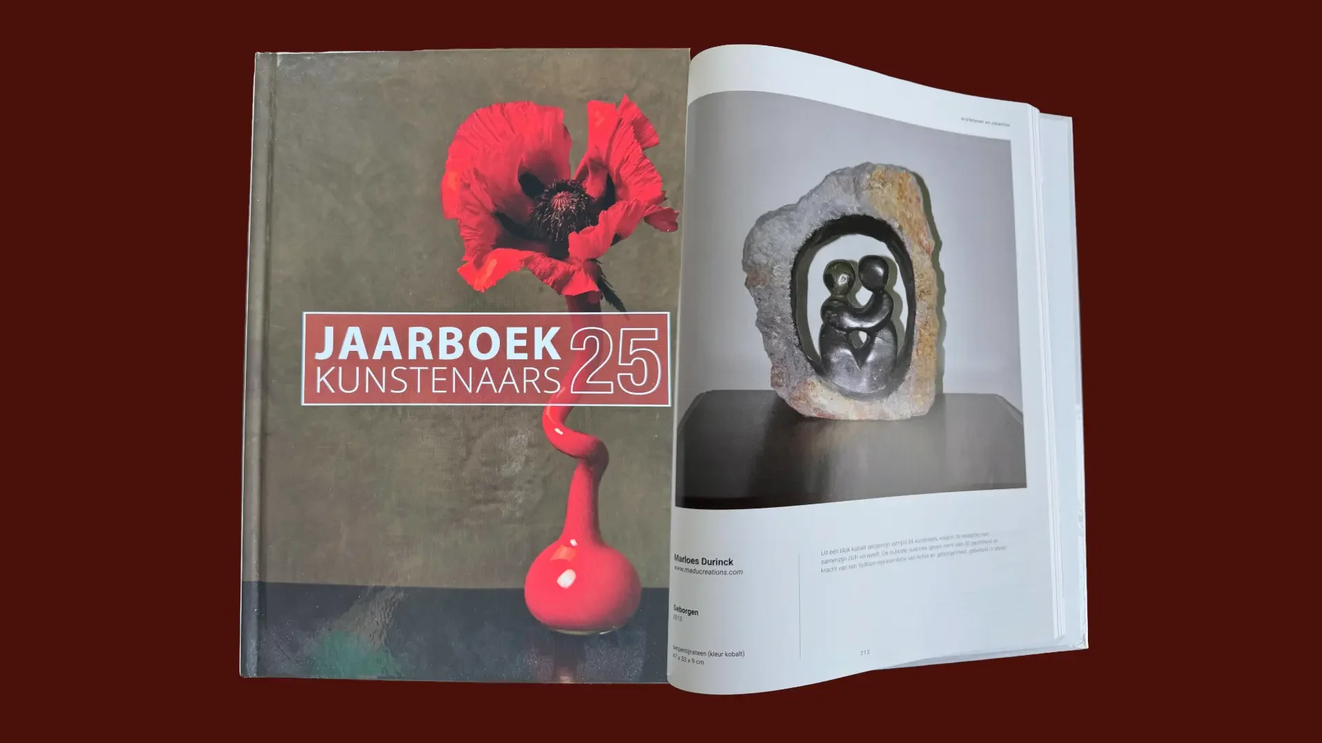 Open jaarboek voor kunstenaars met een rode klaproos op de cover en een foto van een sculptuur in het boek.