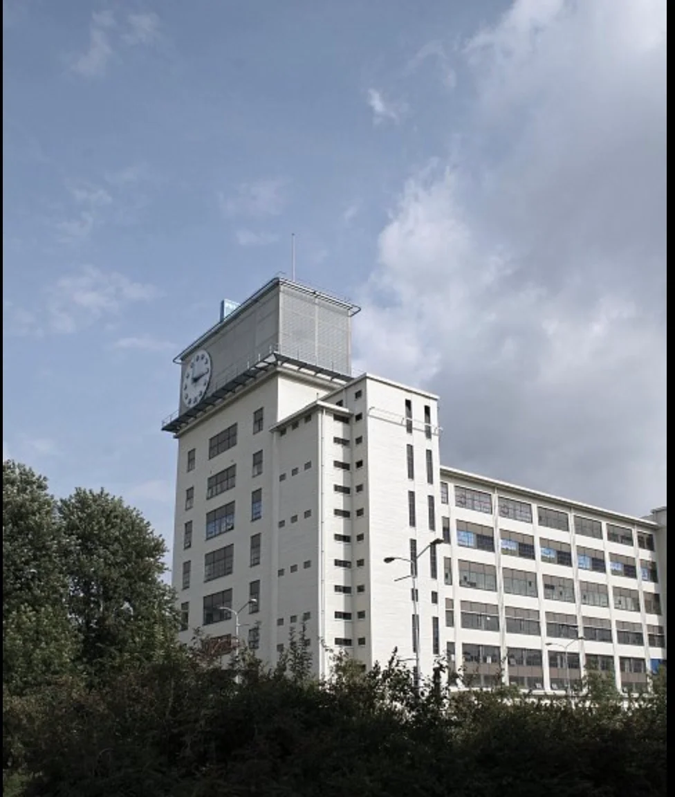 Een wit modern kantoorgebouw met een klok op de top onder een bewolkte hemel.