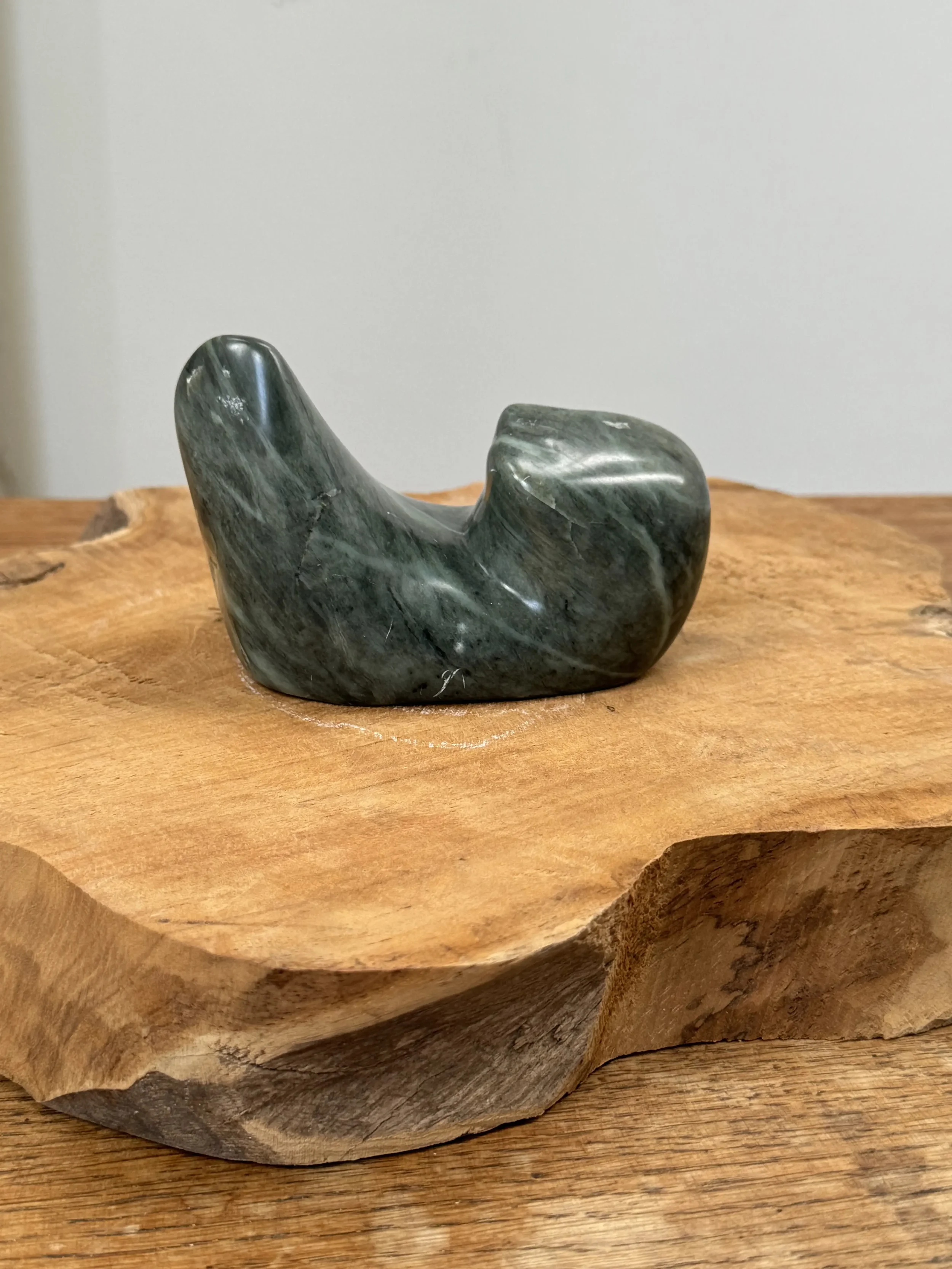 Zeehond van zwarte speksteen gelegen op een houten boomschijf.