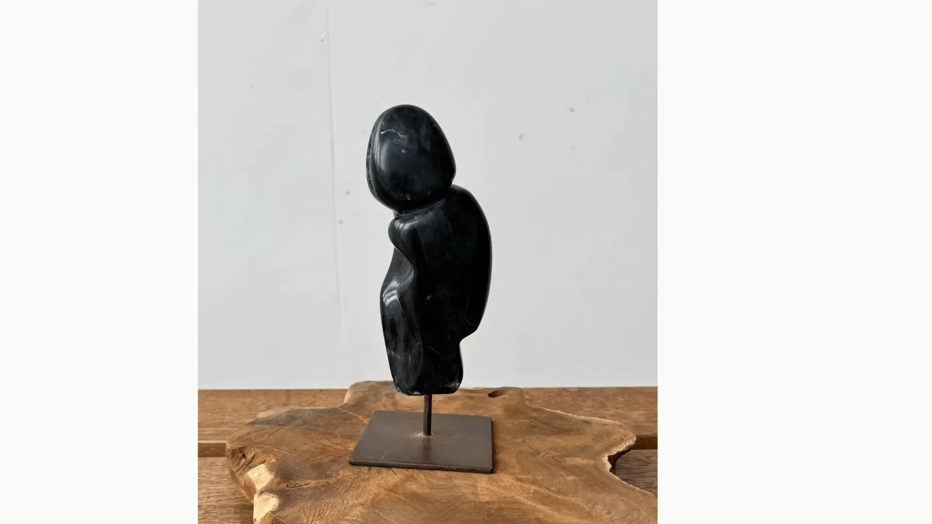 Zwart speksteen beeld op een metalen pin. Uitbeelding van een figuur. Op een houten schijf tegen een witte achtergrond.