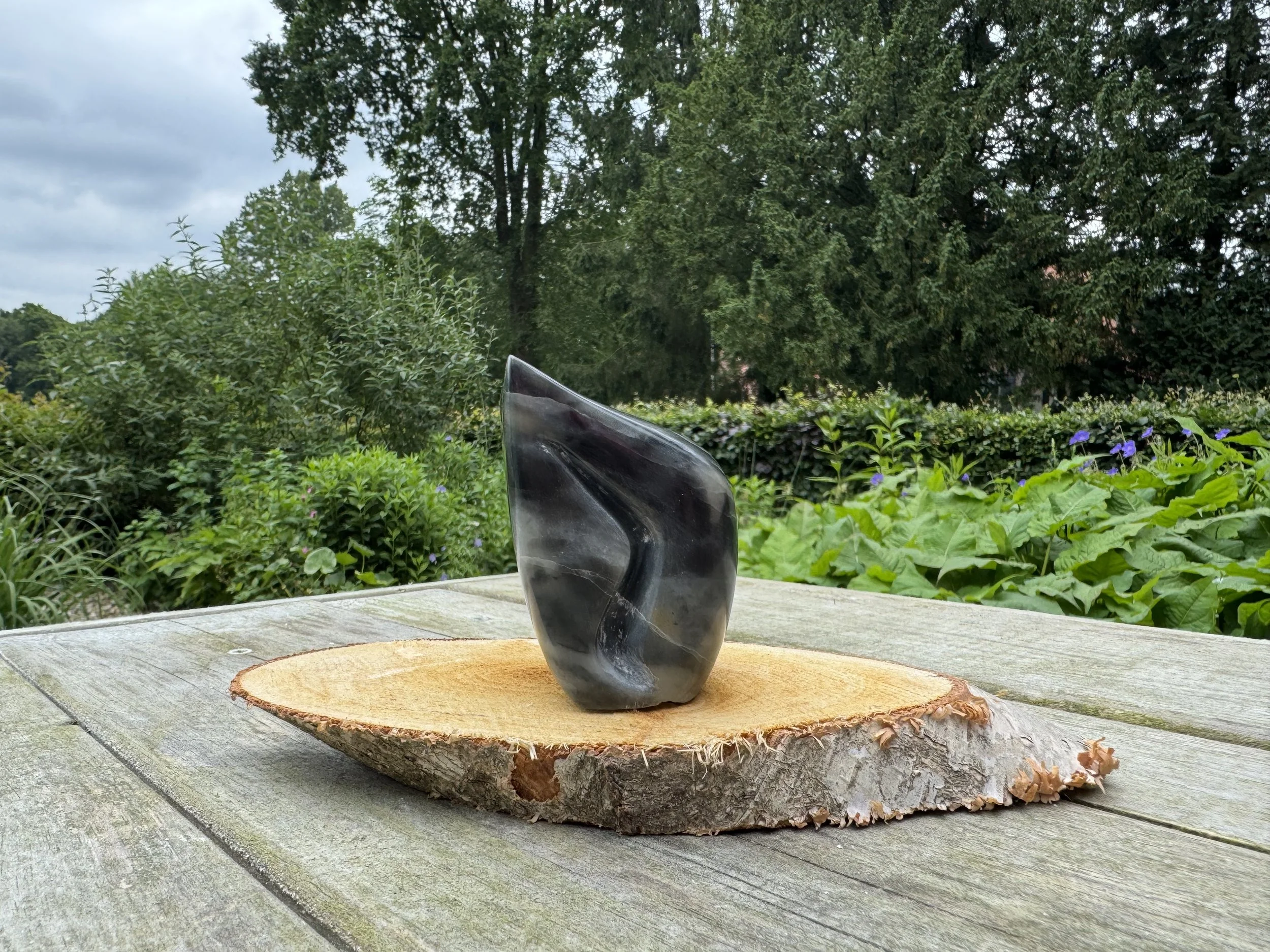 Grijs zwarte Verbinding steen met een verdiepte lijn in het midden op een houten beeldhouwbok met een tuin op de achtergrond