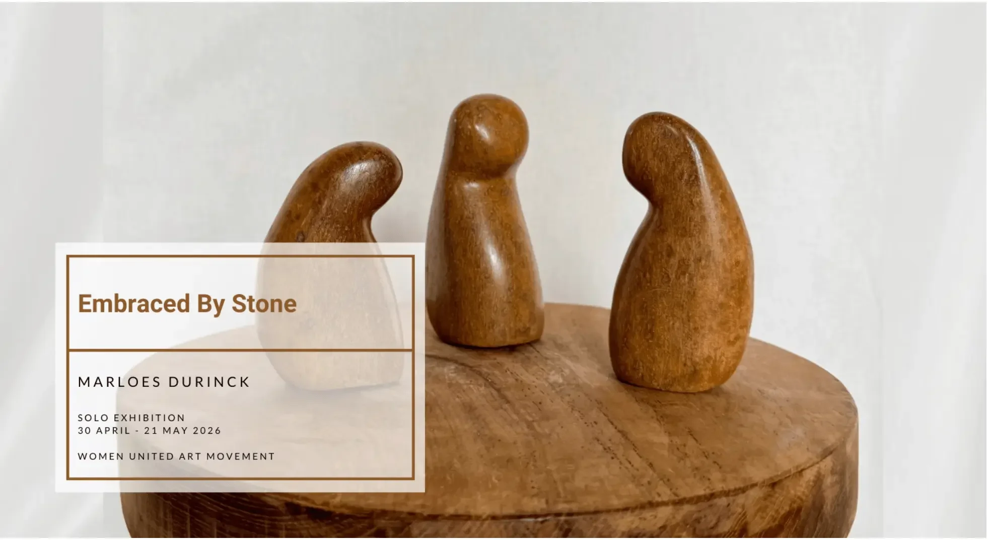 Drie gestileerde stenen sculpturen op een houten tafel met tekst overlay over de linkerkant die zegt "Embraced By Stone" door Marloes Durinck, deel van een solo tentoonstelling van 30 april tot 21 mei 2026 door Women United Art Movement.