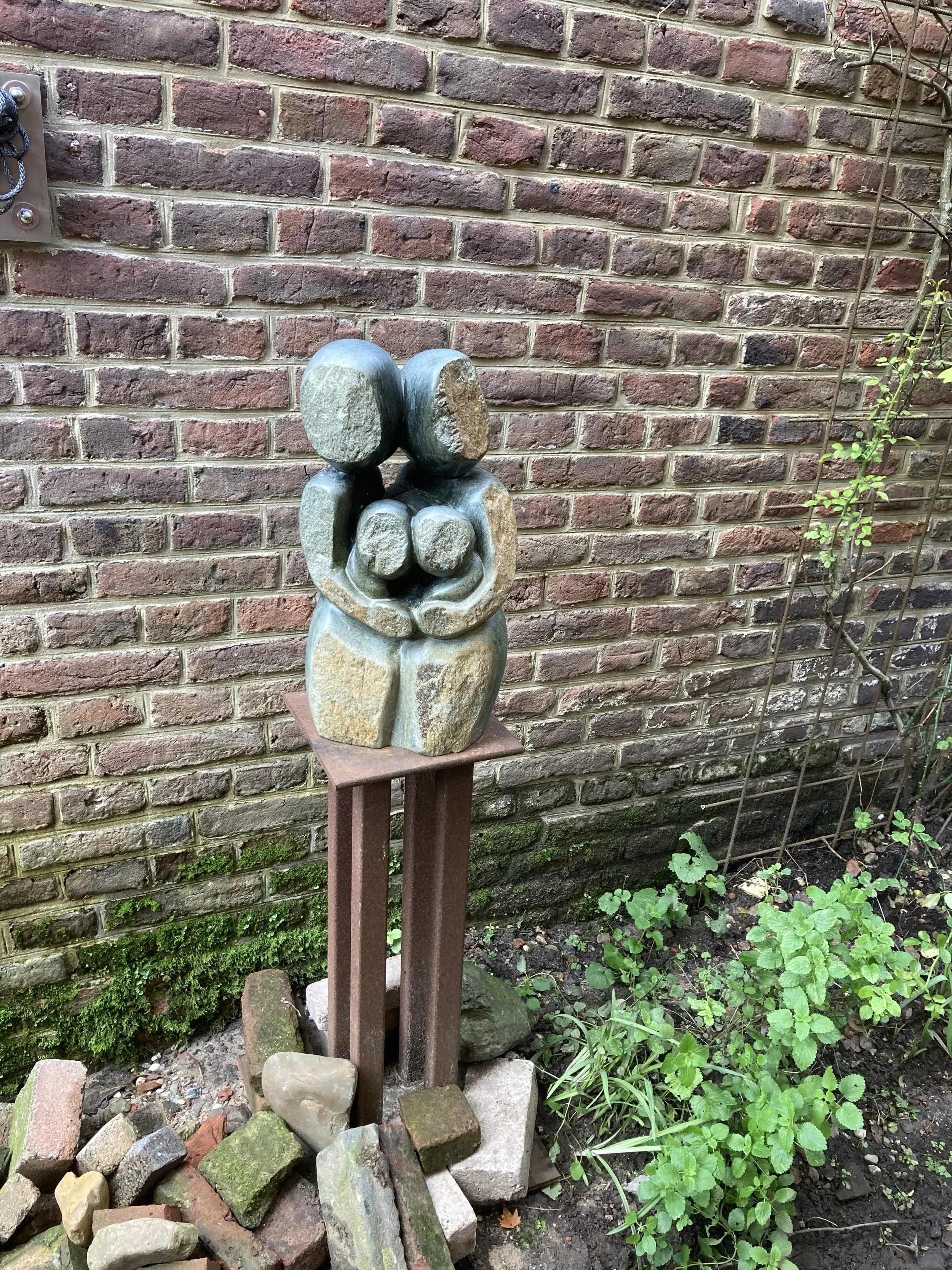 Het beeld Gezin, vier figuren, twee grote die achter twee kleine figuren staan met de armen om hen heen.