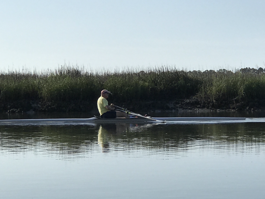 Person rowing on a calm body of water with greenery in the background.