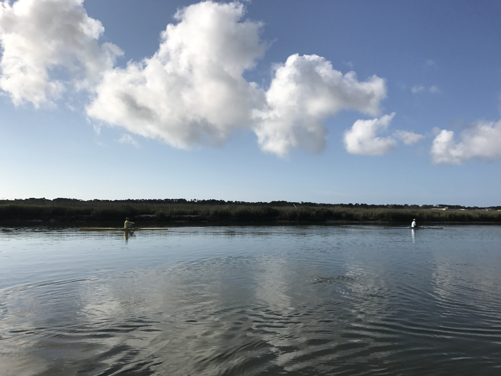 Calm water with two people fishing from small boats under a partly cloudy sky.