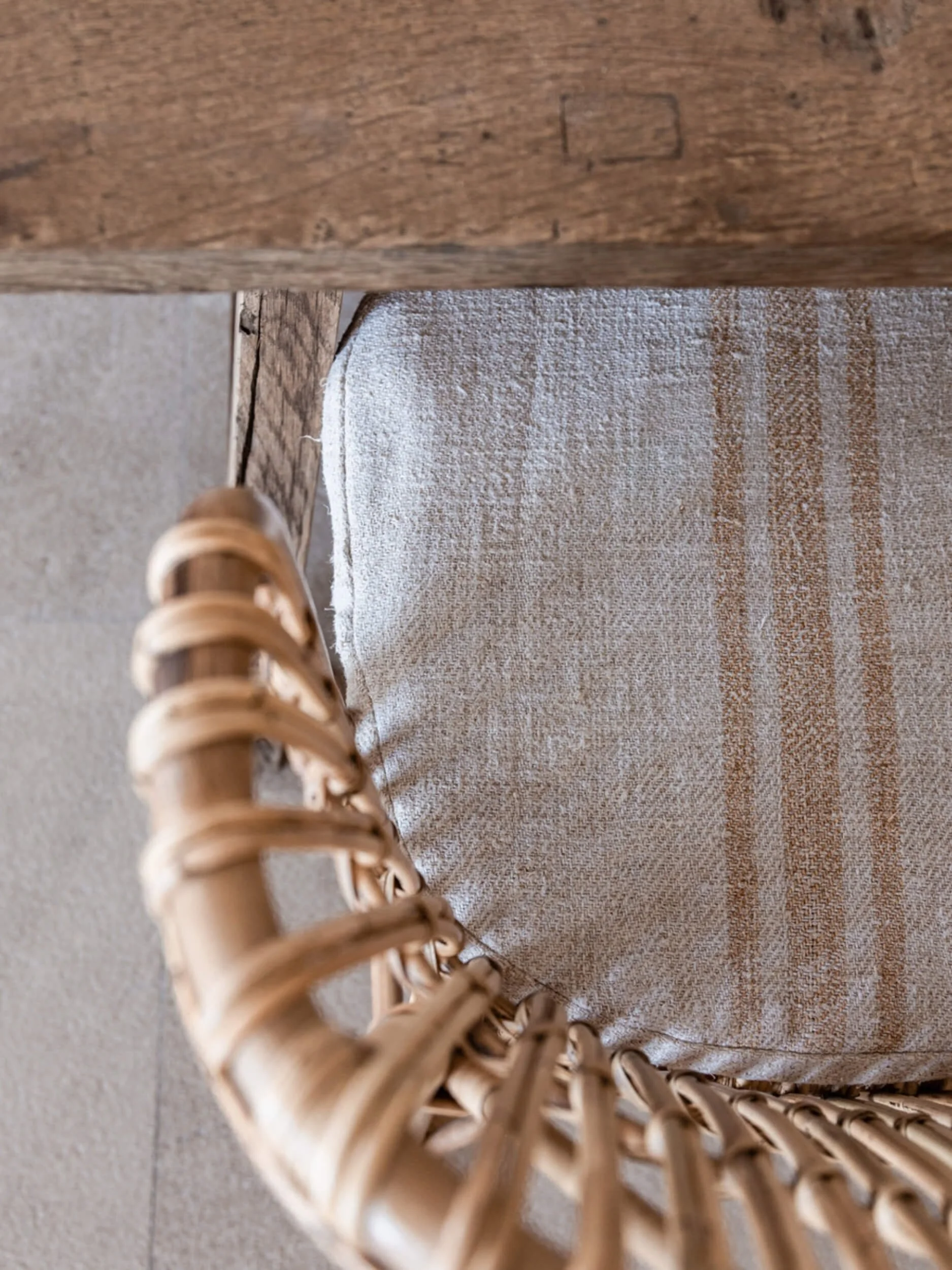 Close-up of a woven wicker chair with a beige and brown striped cloth underneath and a wooden table leg in the background.