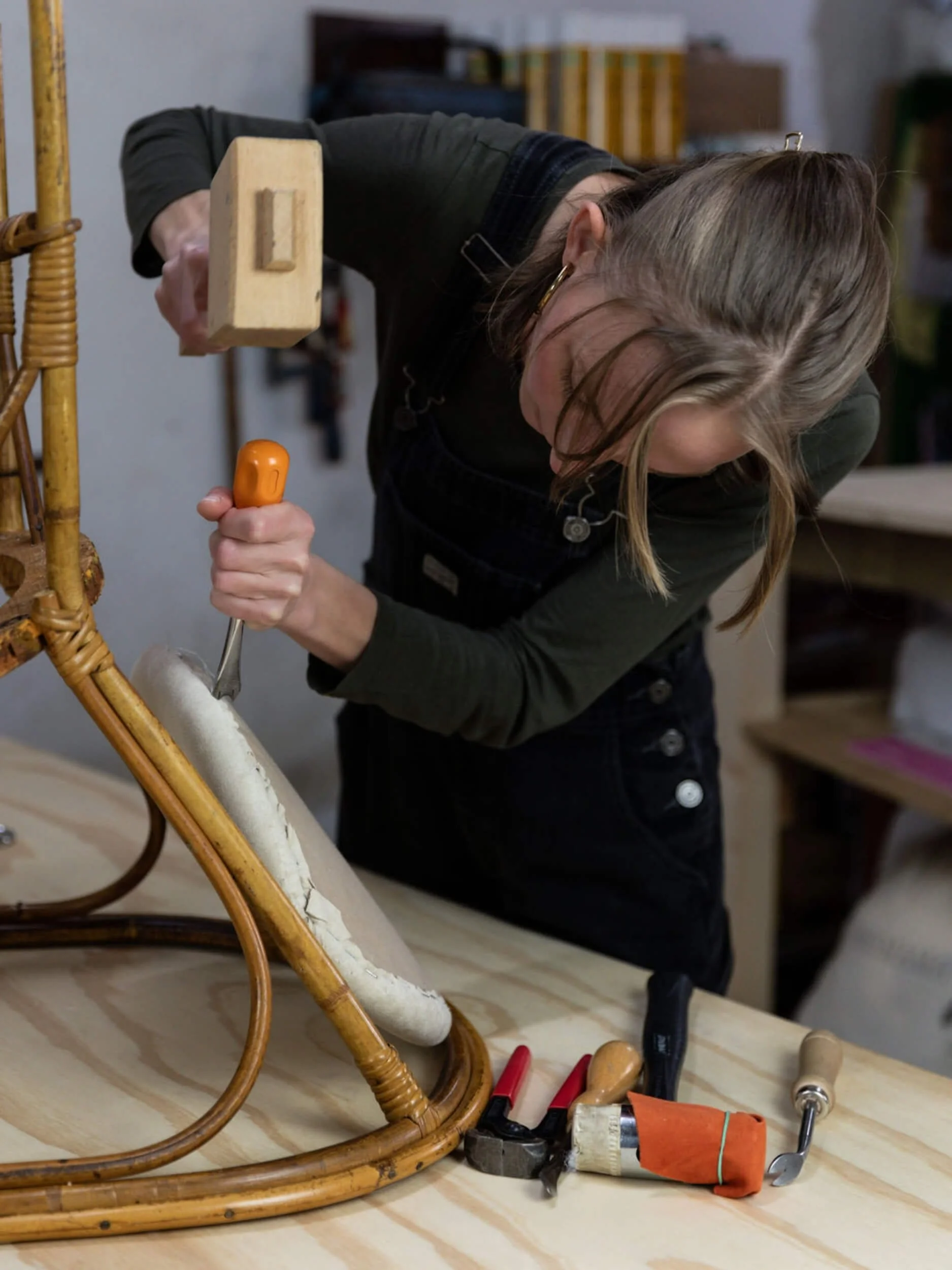A woman tightening a screw in a wicker chair with various tools lying on a wooden table.