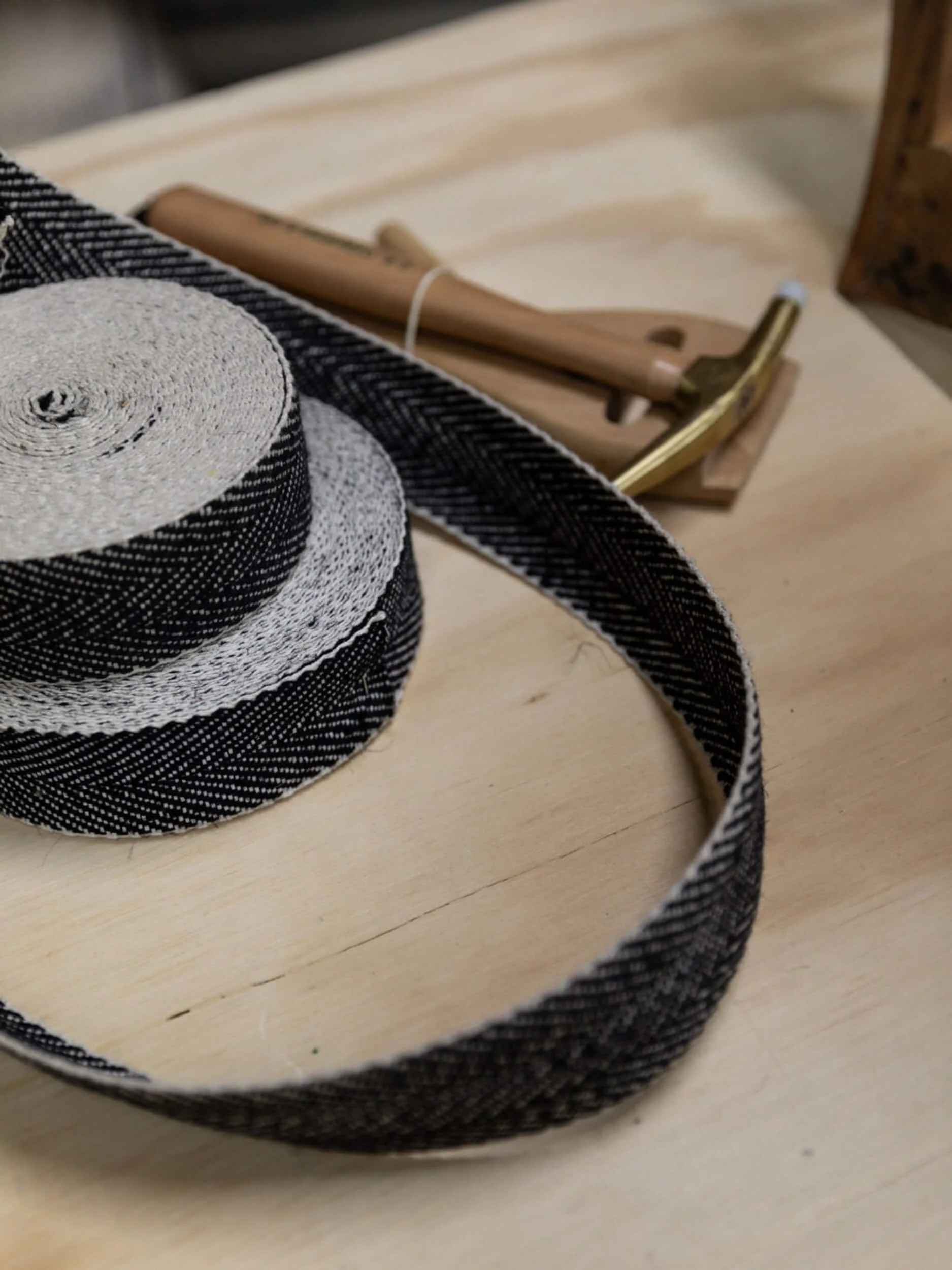 A black and white striped ribbon, a wide-brimmed woven sun hat, and a pair of wooden and metal sunglasses on a light wooden surface.