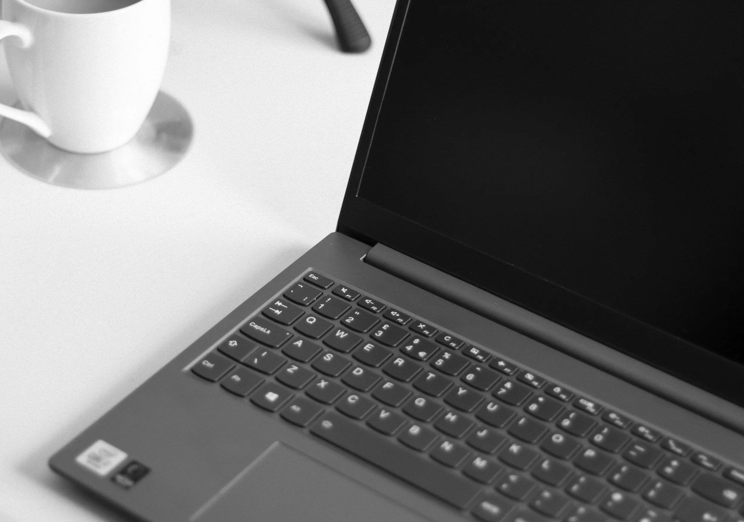 Schwarz-weißer Laptop mit sichtbarer Tastatur auf einem weißen Tisch, neben einer weißen Kaffeetasse.