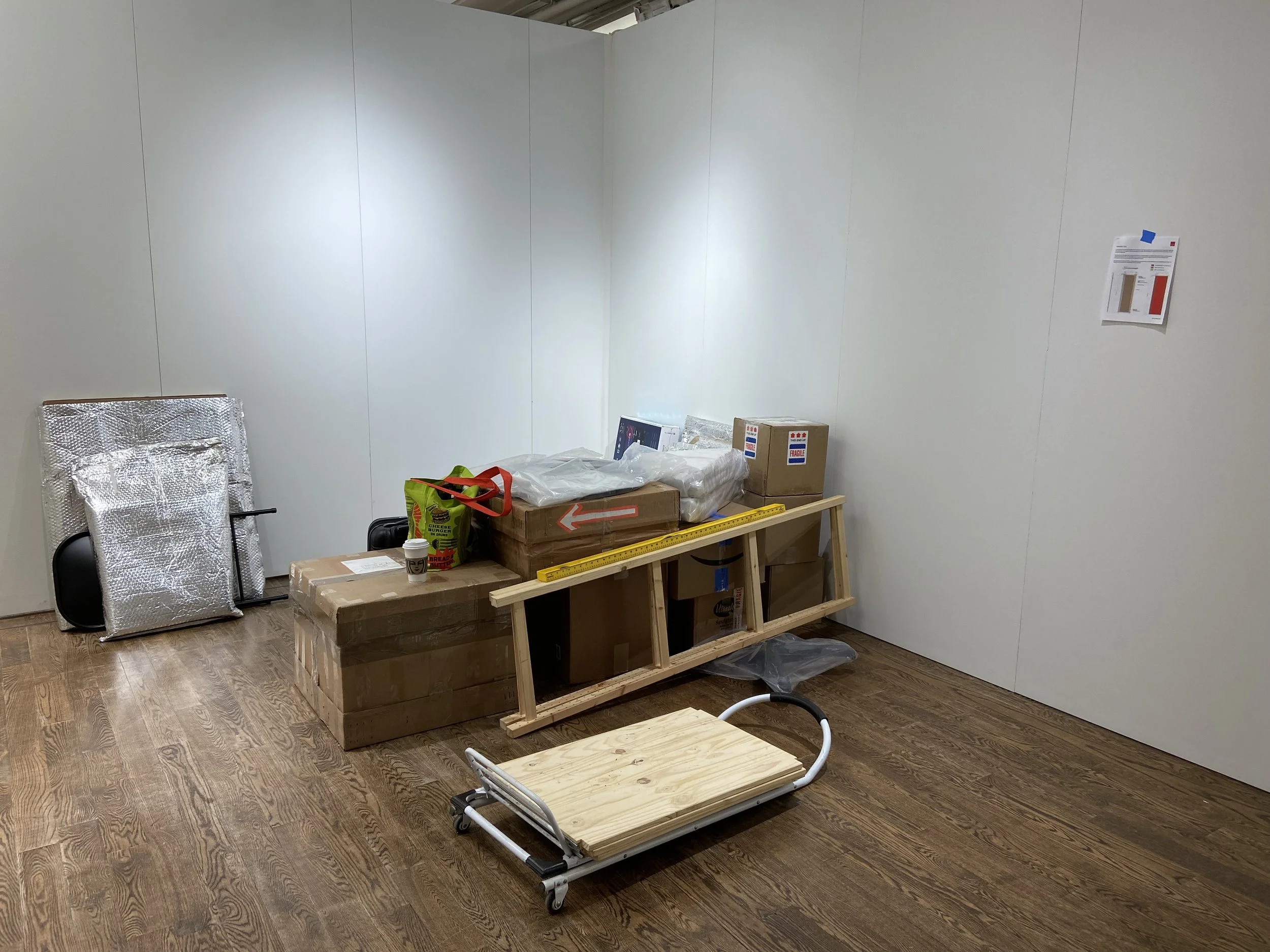 An unfinished room with a white wall, construction materials, boxes, and a wooden platform on wheels.
