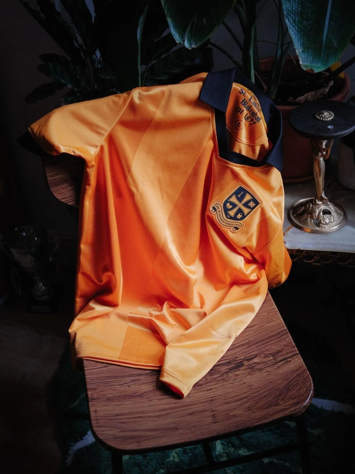 An orange and black sports jacket with a patch on the sleeve, resting on a wooden table.