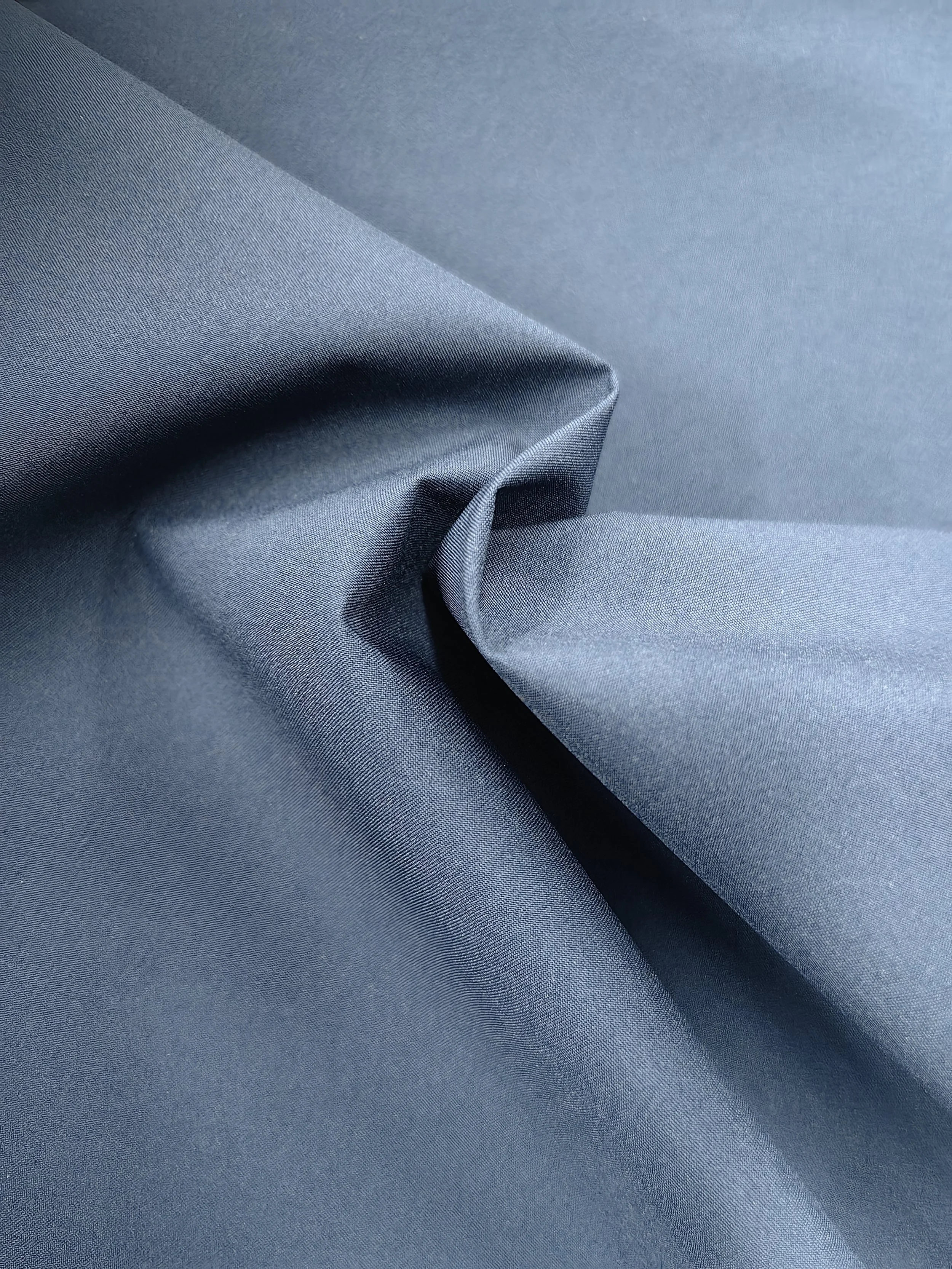 Close-up of smooth, blue fabric with a slight sheen, showing gentle folds and texture.