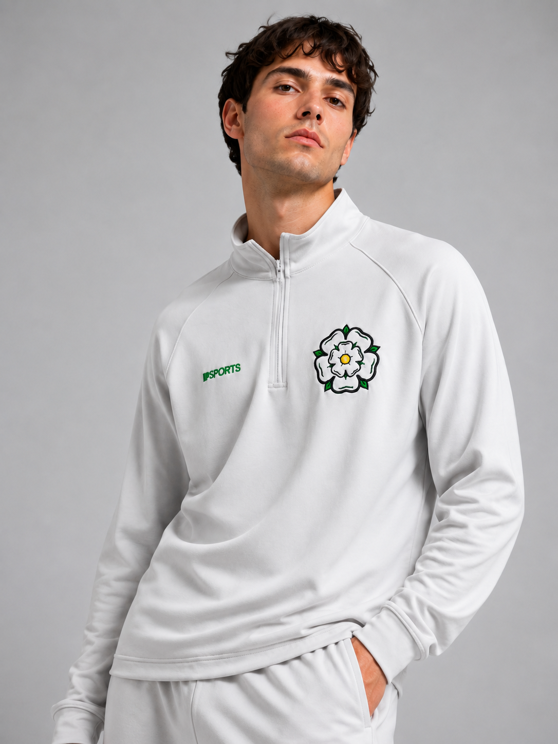 Young man wearing a white athletic jacket with a black and white rose emblem and green lettering, standing with one hand in his pocket against a gray background.