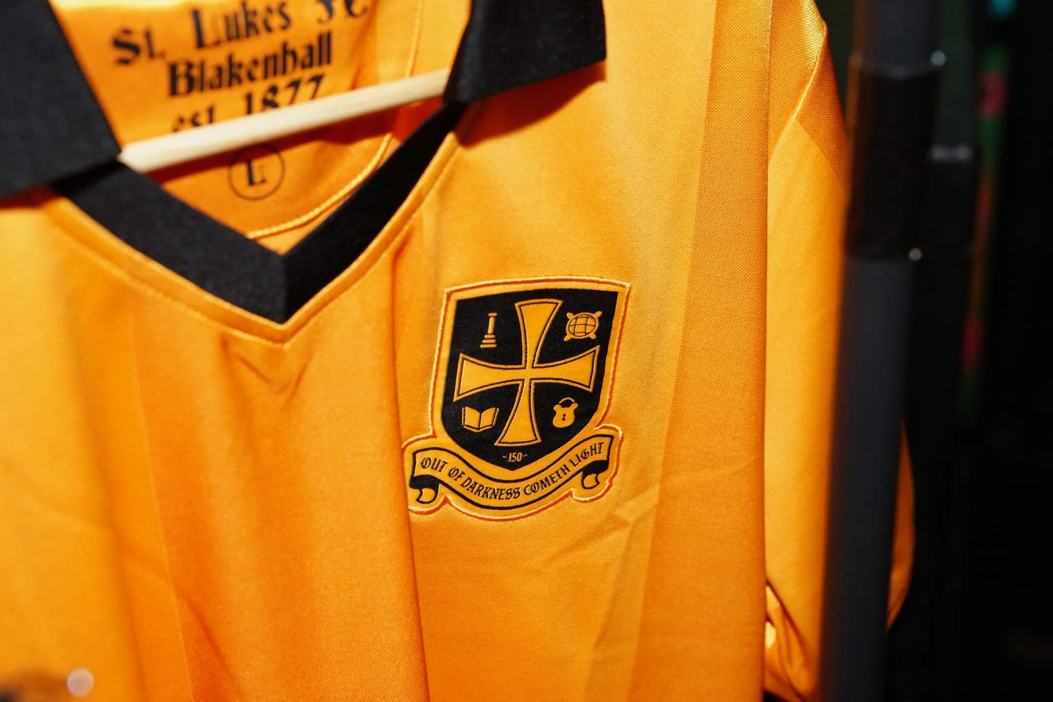 Close-up of an orange sports jersey with a black and orange team logo and a black collar, hanging on a hanger.