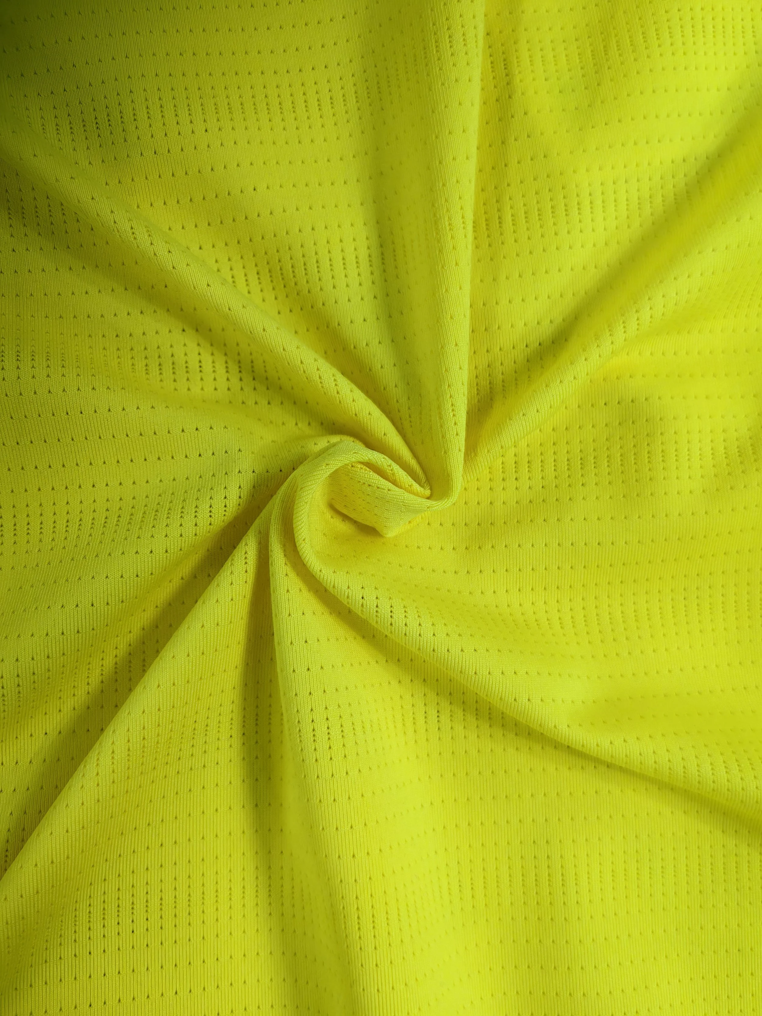 Close-up of bright yellow fabric with small perforations, gathered and twisted in the center.