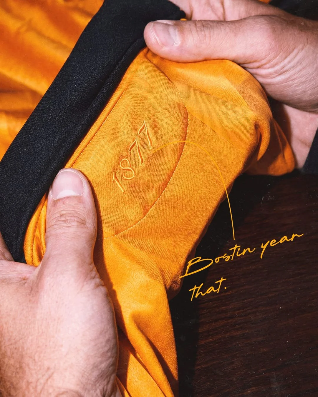 Close-up of a person holding a yellow-orange fabric item with the embroidered number 1071, and a handwritten note pointing to it saying "Bootin year that."