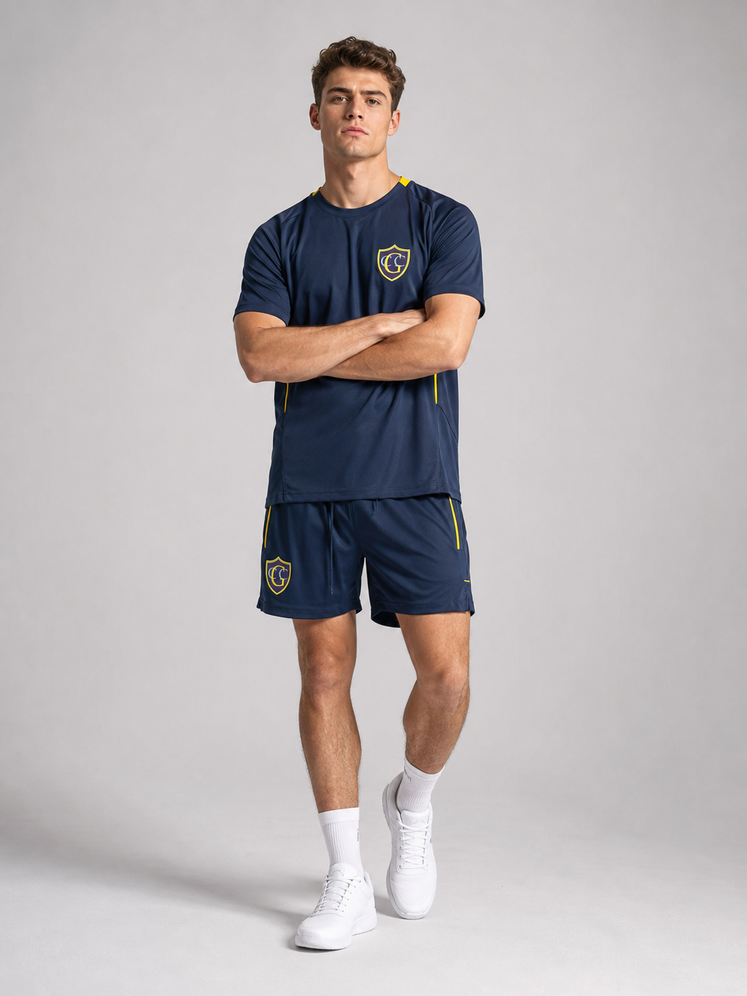 Young man in navy blue sportswear with yellow accents, standing with arms crossed against a plain gray background.