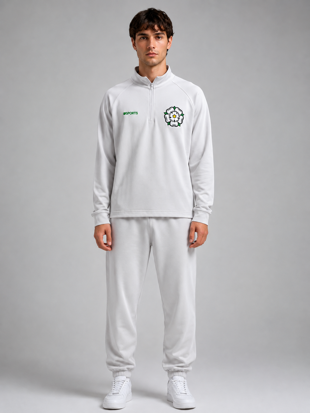 Young man in white tracksuit with sports logos, standing against a plain gray background.